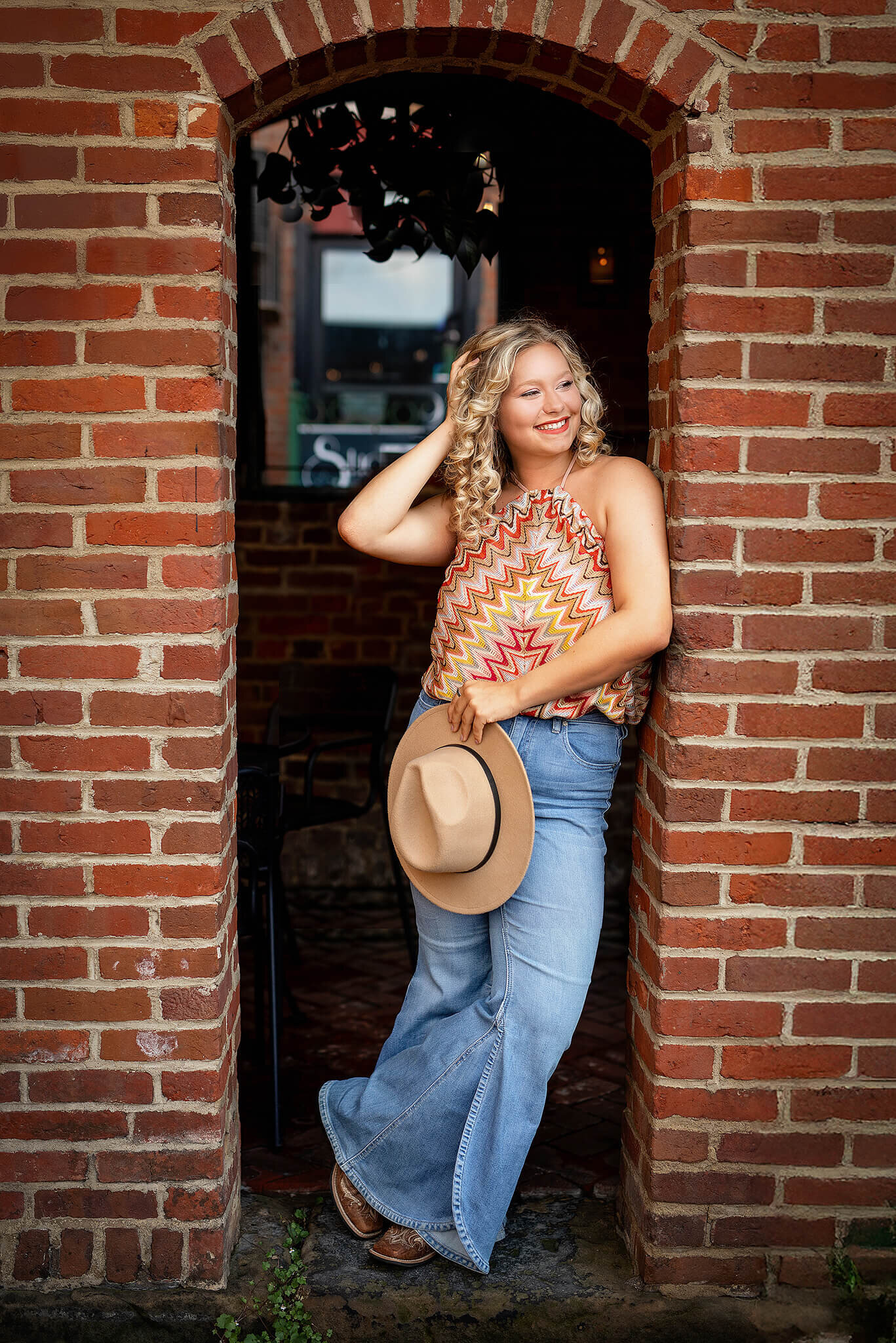 Colonel Crawford high school senior standing in a brick doorway while holding hat and looking off to the side