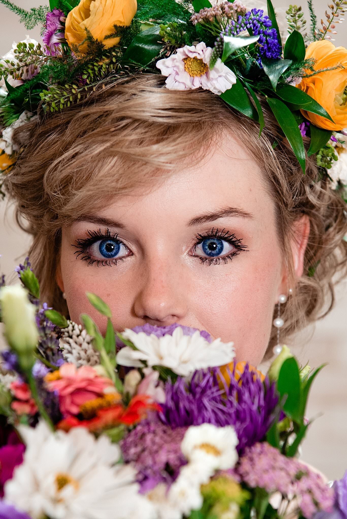 Close up photo of bride with bright blue eyes and surrounded by bright wildflowers in her bouquet and crown