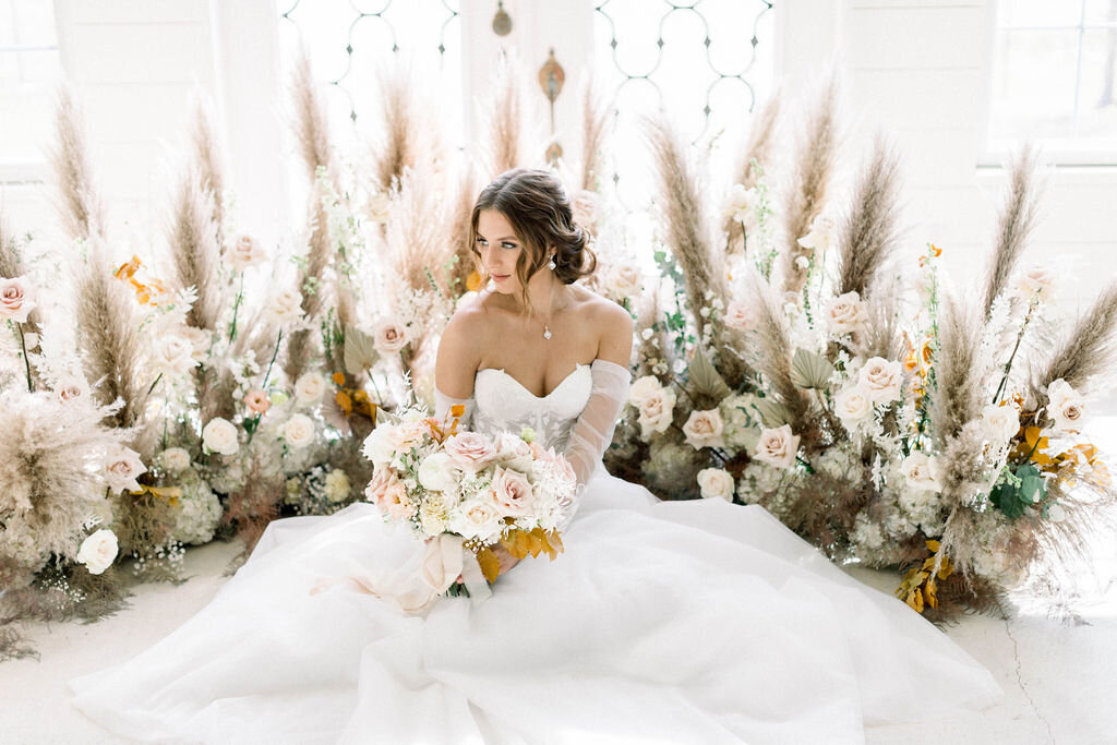 A gorgeous bride sitting down in her wedding dress in front of a floral arrangement