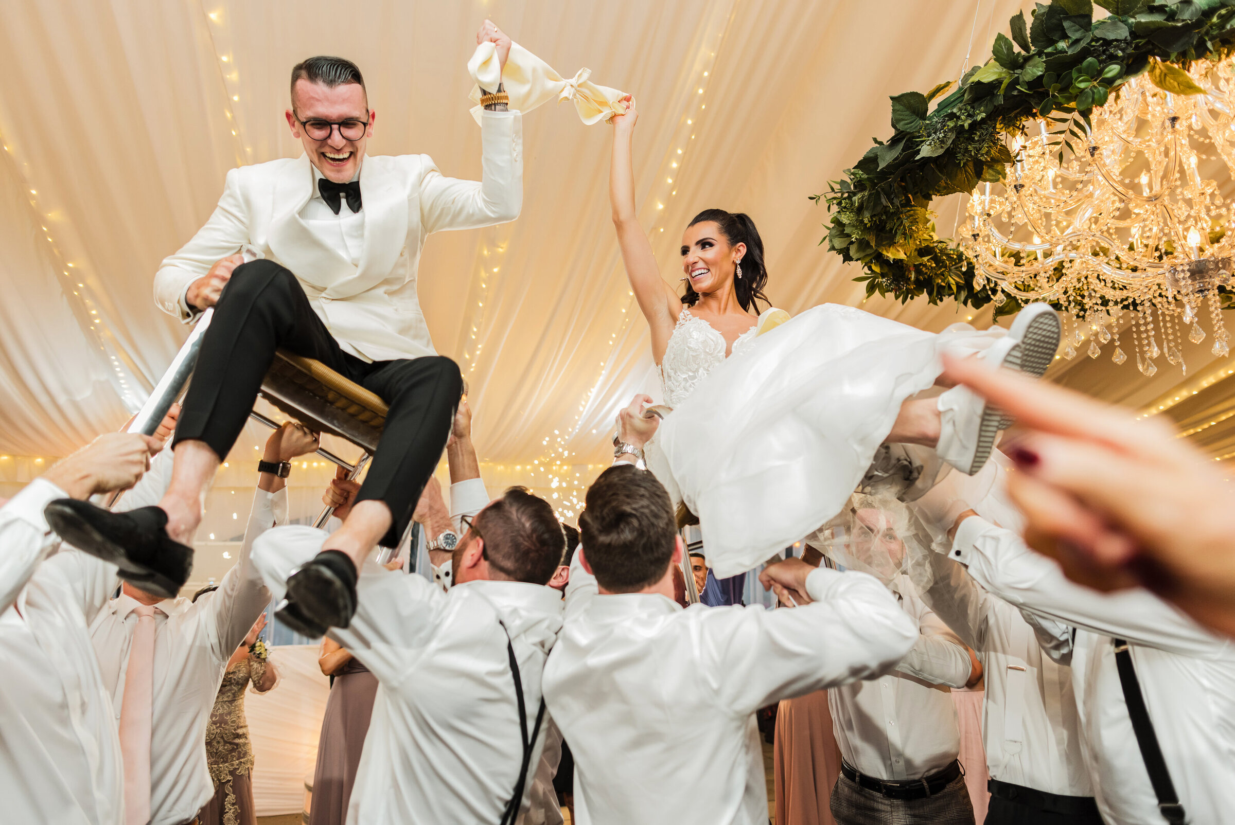 Bride and groom laughing lifted on the chairs during Jewish hora at Water Works wedding reception