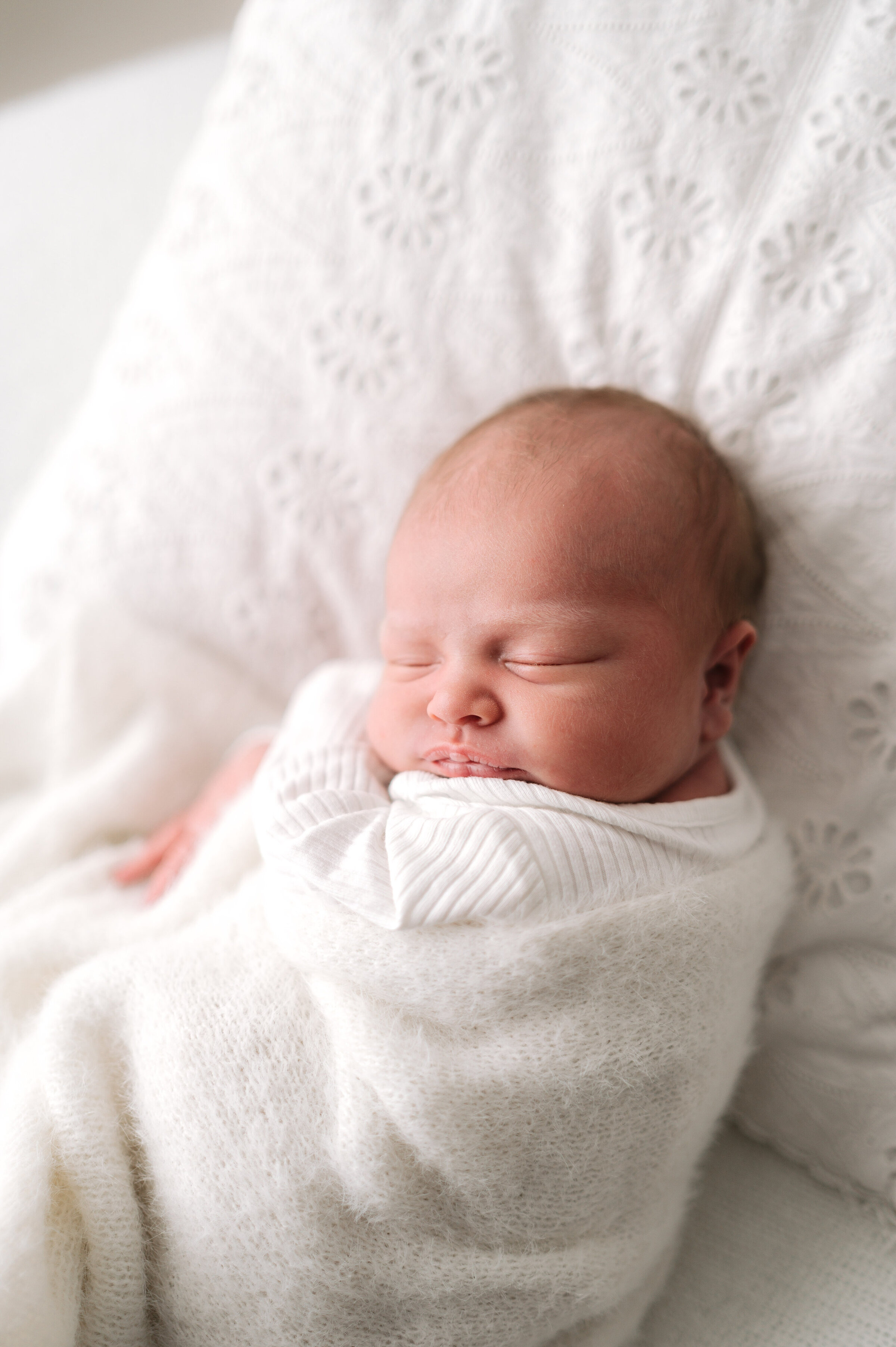 A baby swaddled up sleeping on a white pillow at newborn photoshoot in Billingshurst