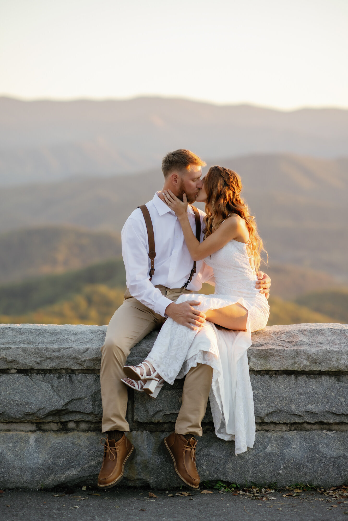 Gatlinburg elopement with bride and groom in the Foothills Parkway sitting on a stone wall together and kissing during a sunset