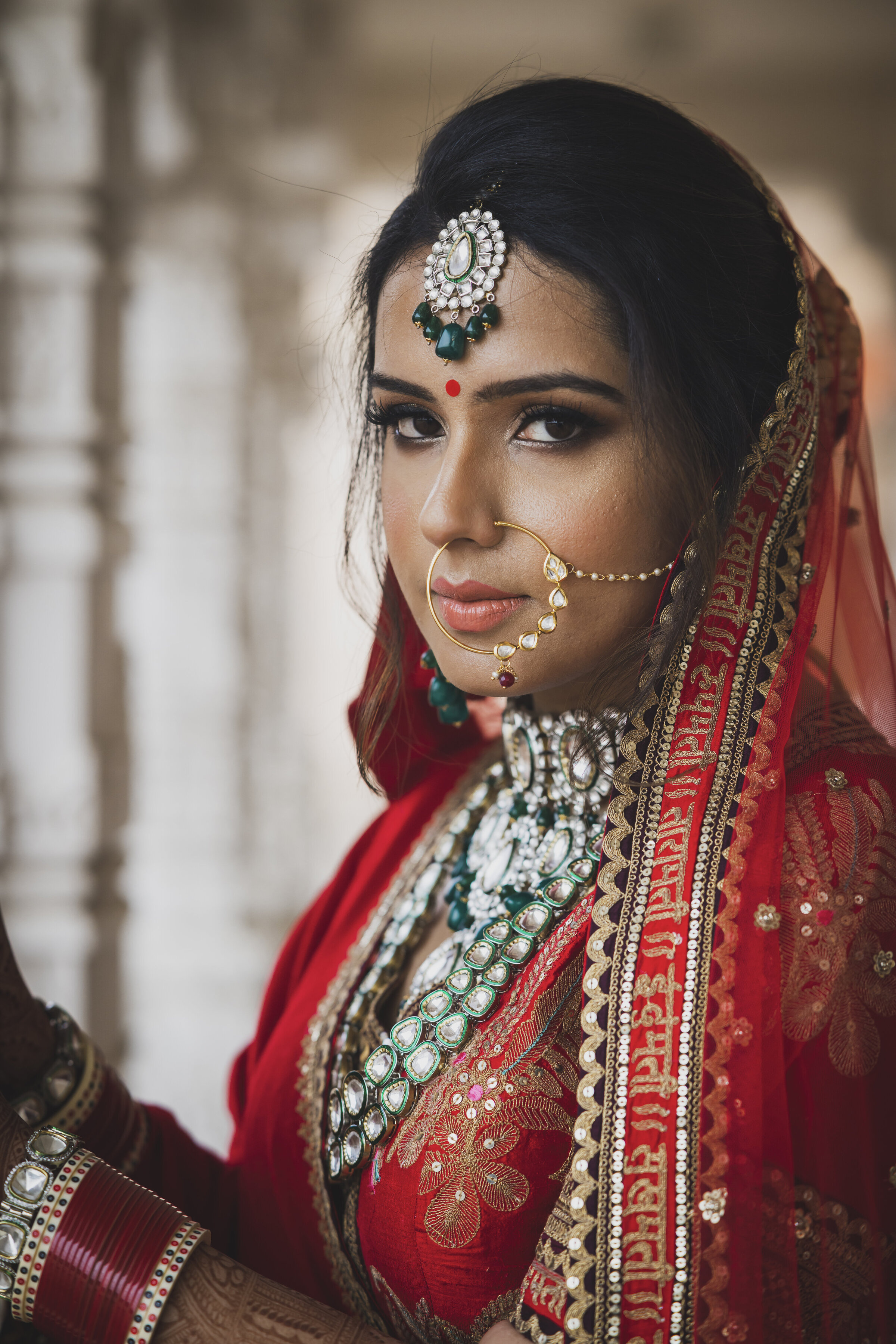Indian bride with nose ring attached to ear looks at camera.
