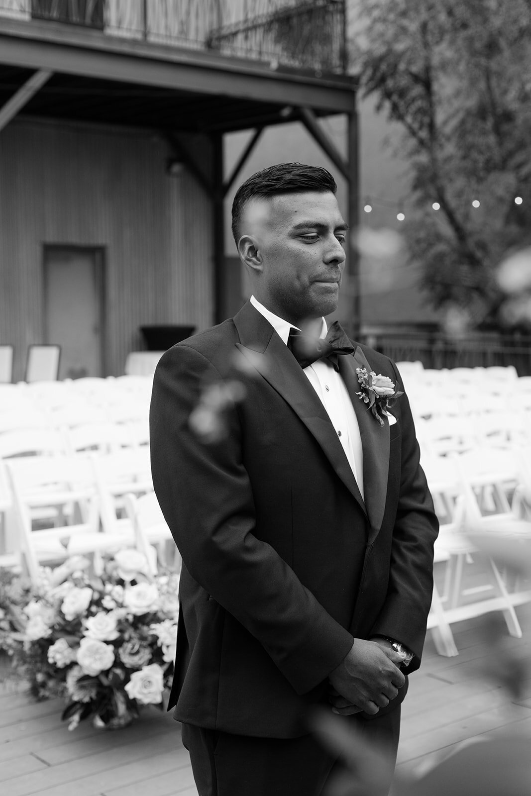 Groom standing in a sea of white ceremony chairs at an outdoor garden wedding venue in Austin, captured in a timeless black and white portrait before seeing his bride