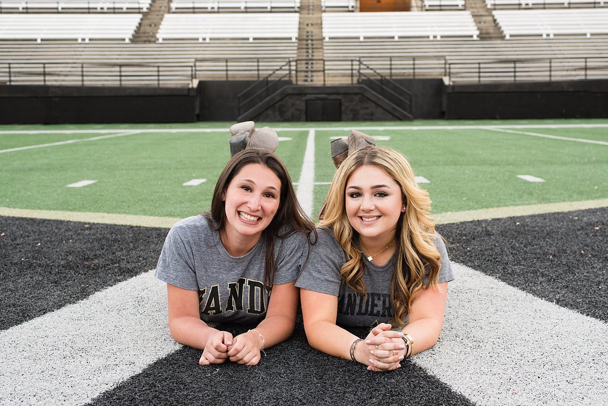 College senior photoshoot of 2 roommates lying on their stomachs side by side smiling at the camera on the football field