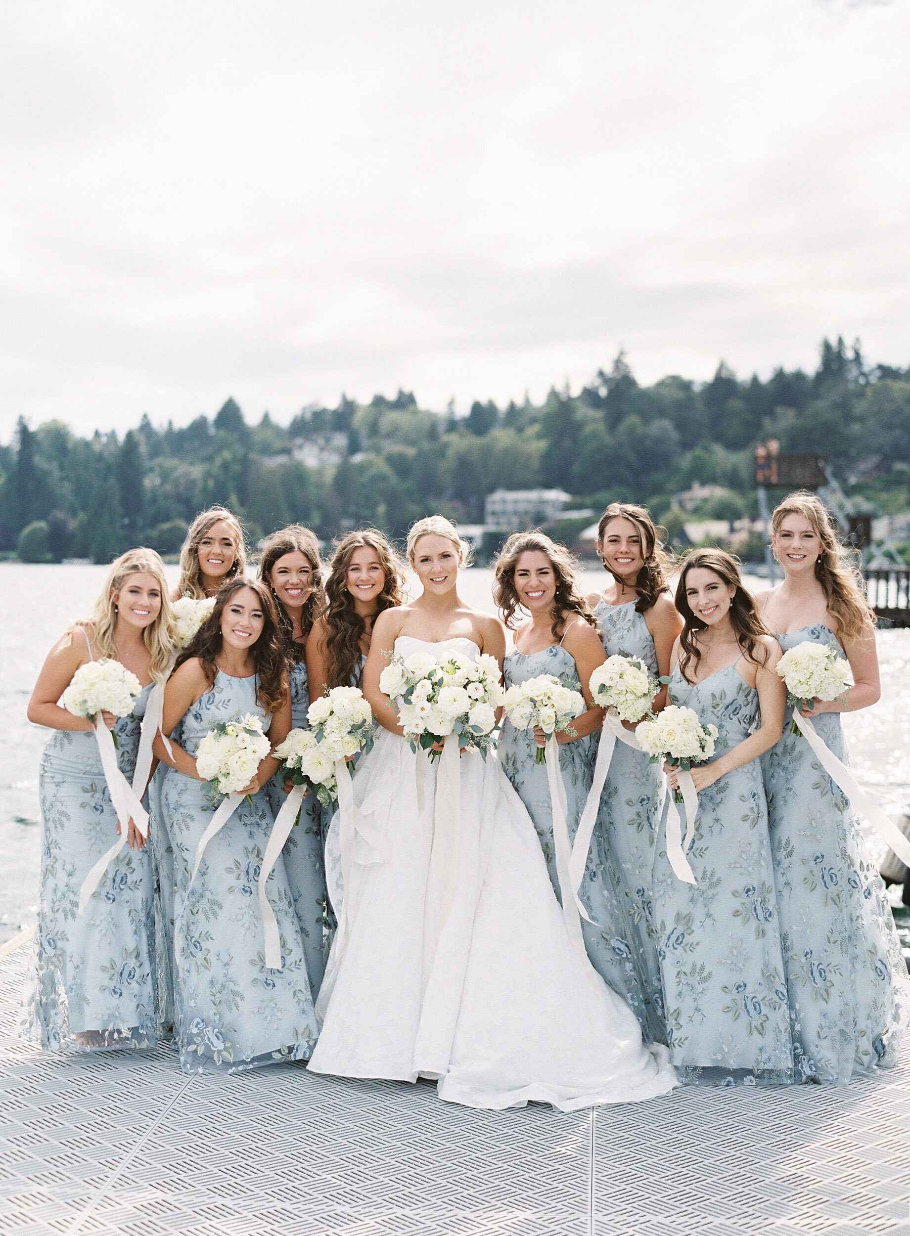 bridesmaids in long light blue floral dresses with bride on dock on lake washington