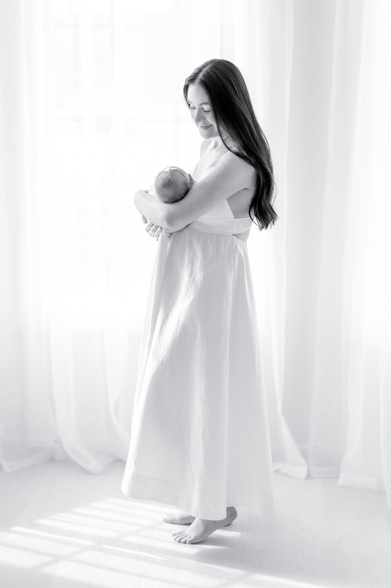 black and white image of a woman holding a newborn in front of a window  in Kristie Lloyd's Nashville newborn photography studio