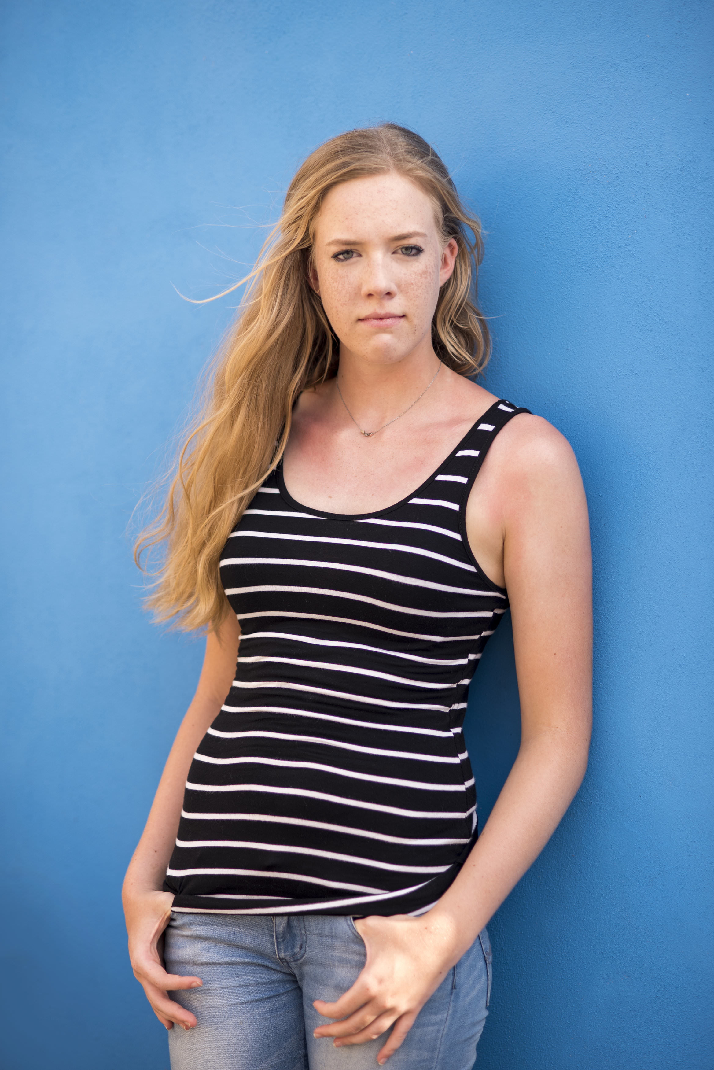 Senior Photo in front of bright blue wall wearing striped black and white tank top and jeans
