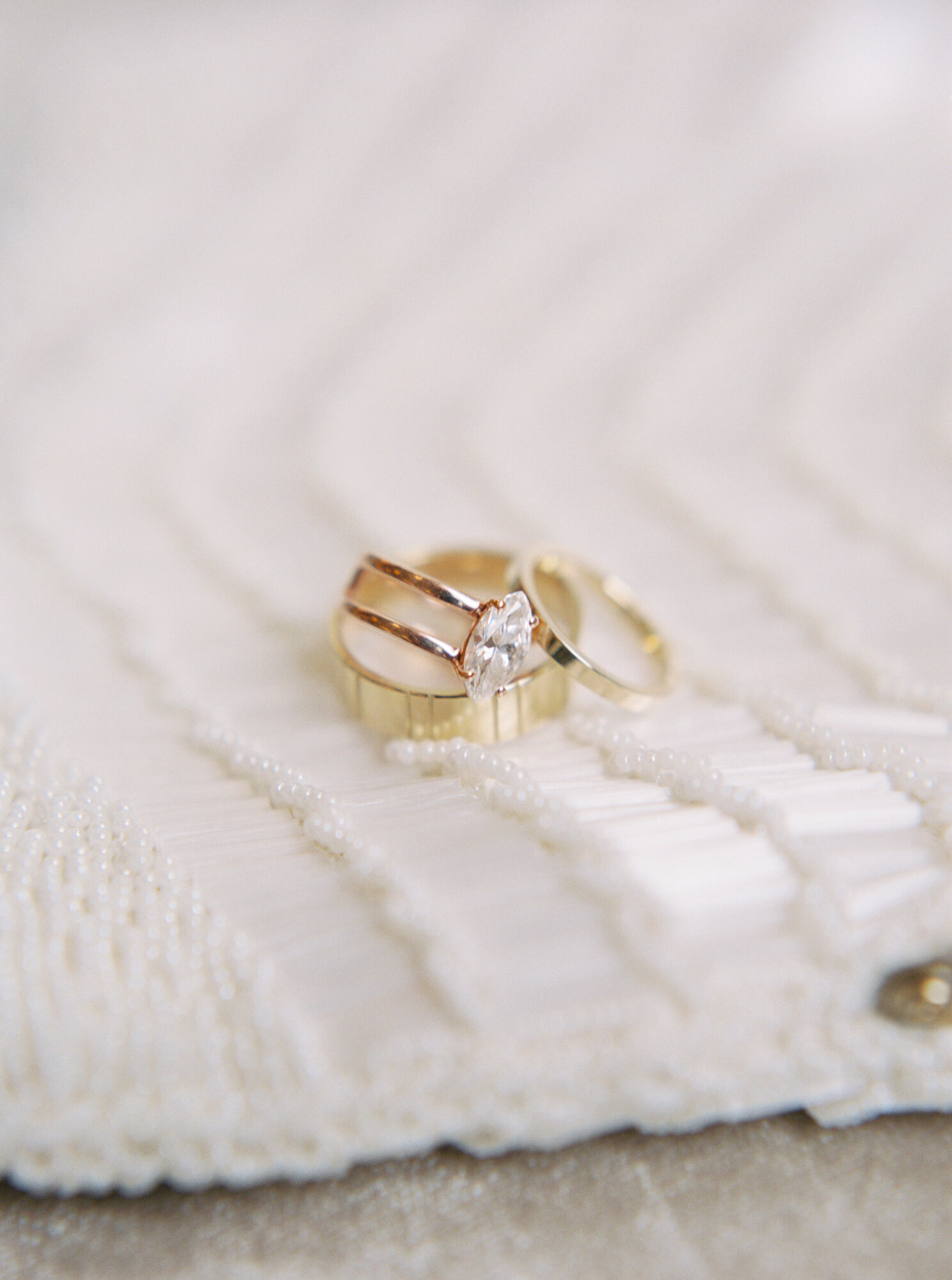 gold diamond engagement ring and wedding band on pearl handbag macro photo