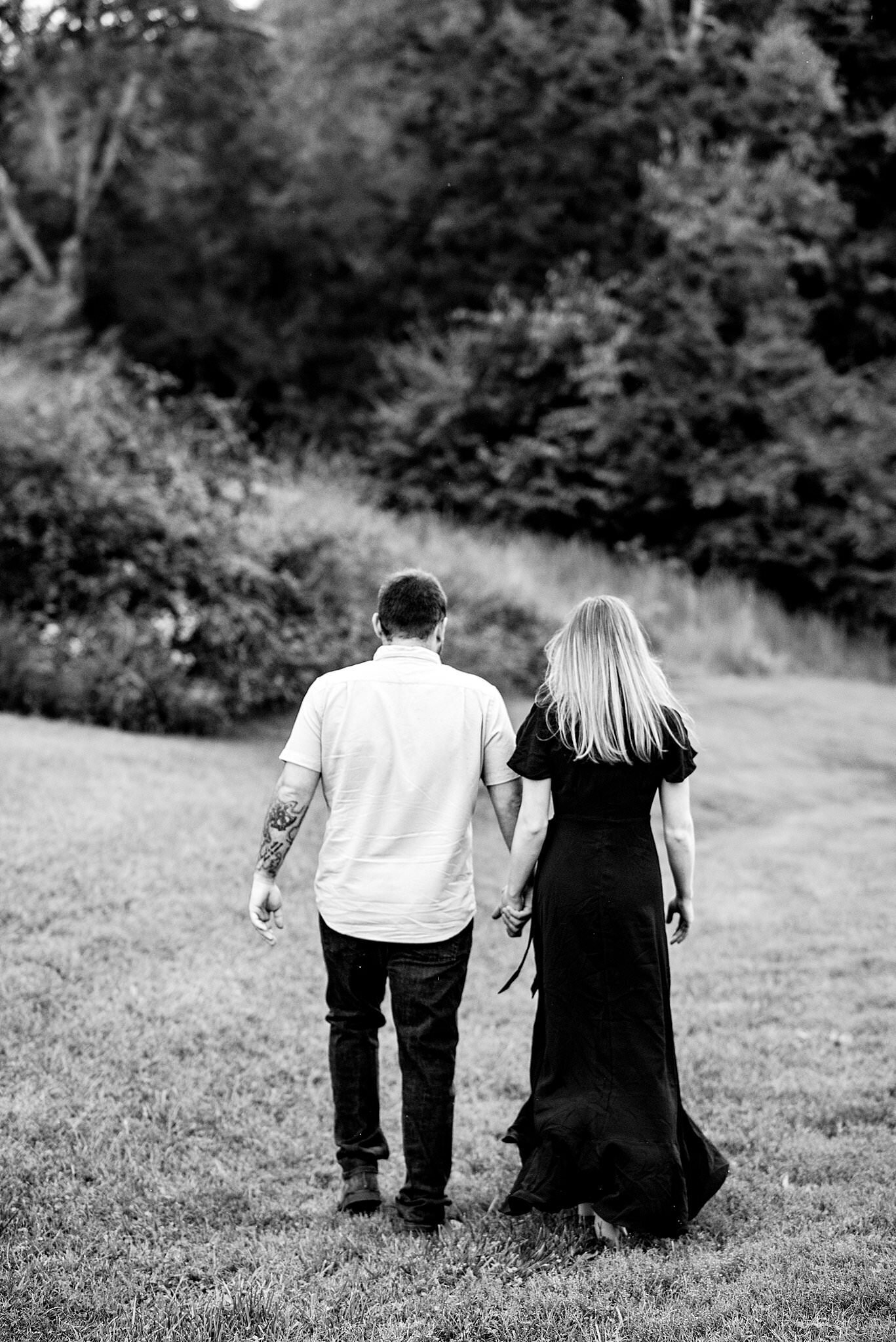 Black and white portrait of couple holding hands and walking through a field