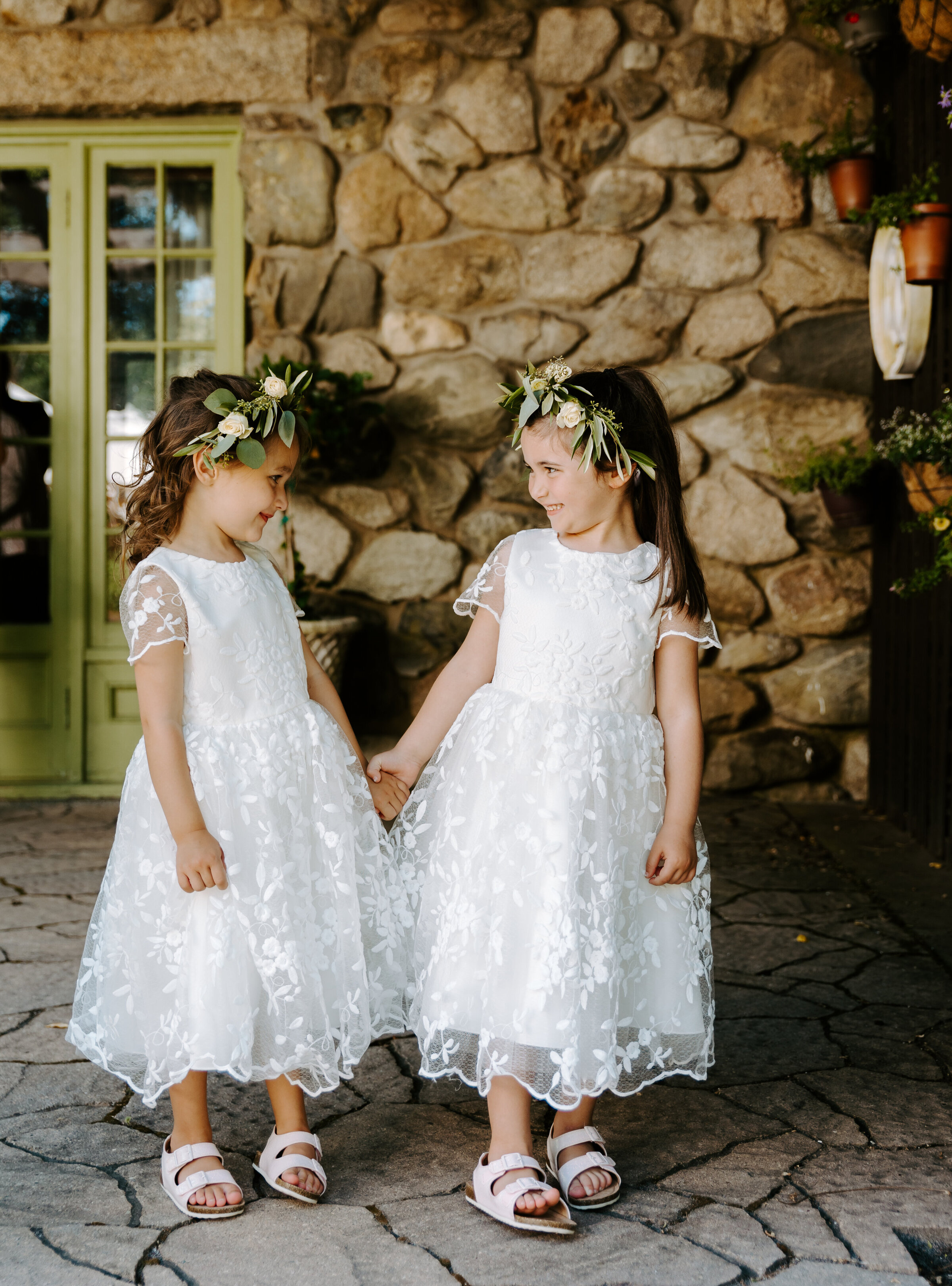 Two little flower girls hold hands and smile at each other before wedding ceremony at The willowdale Estate in Topsfield, Massachusetts