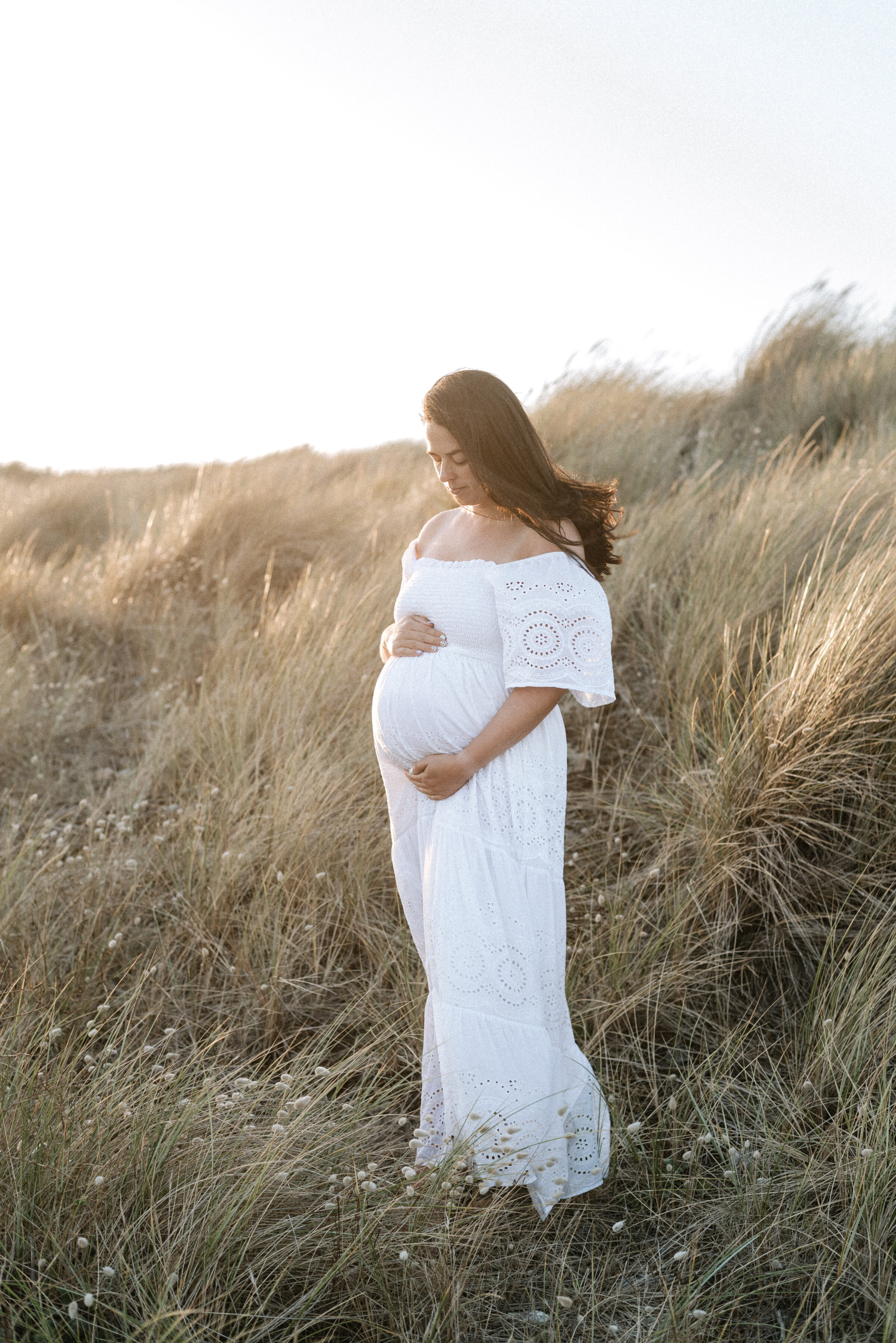 Pregnant women standing in a field at sunset at maternity photoshoot in Billingshurst