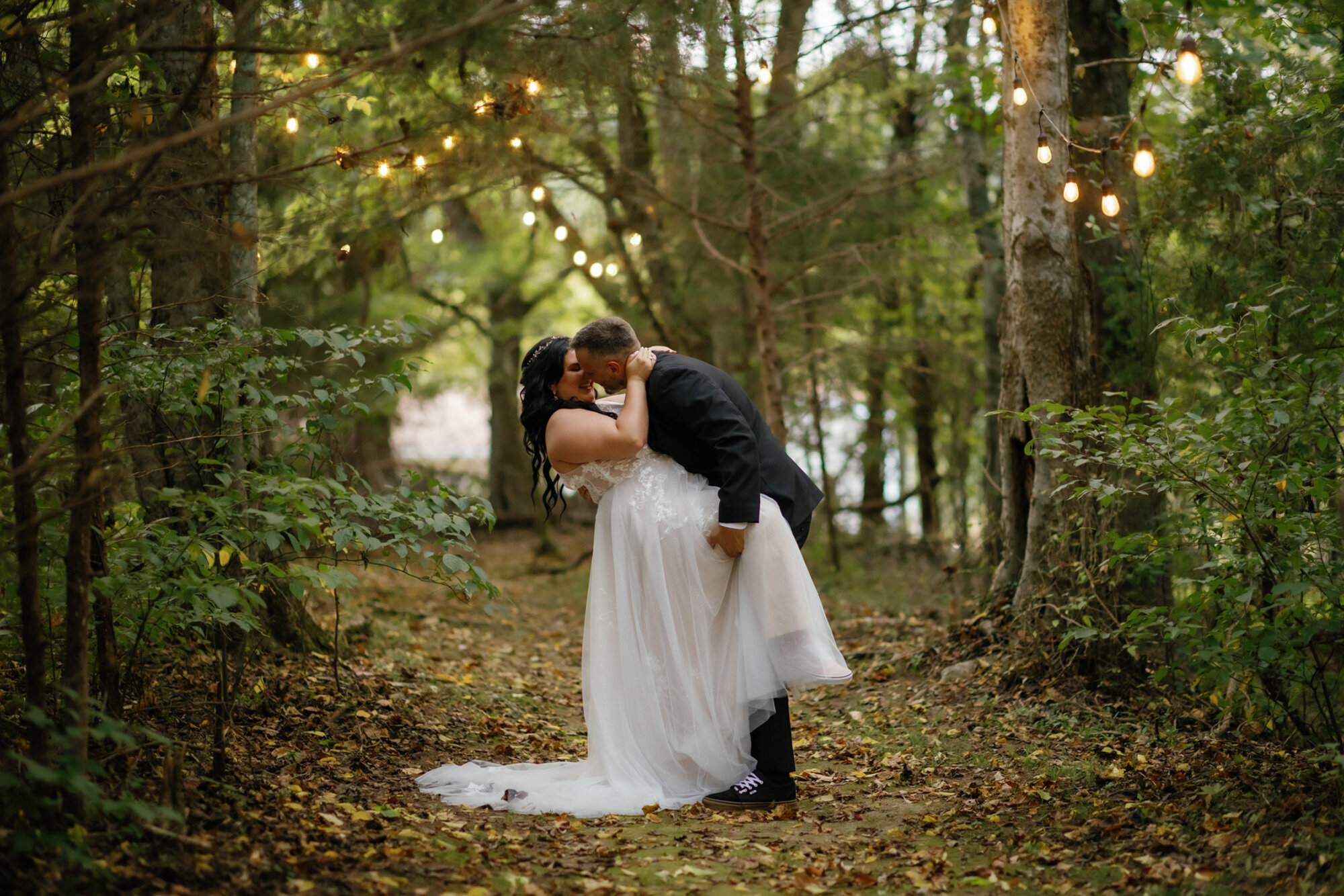 woodland wedding in the Smokies with groom dipping his bride backwards with her leg up and kissing her with string lights through the trees