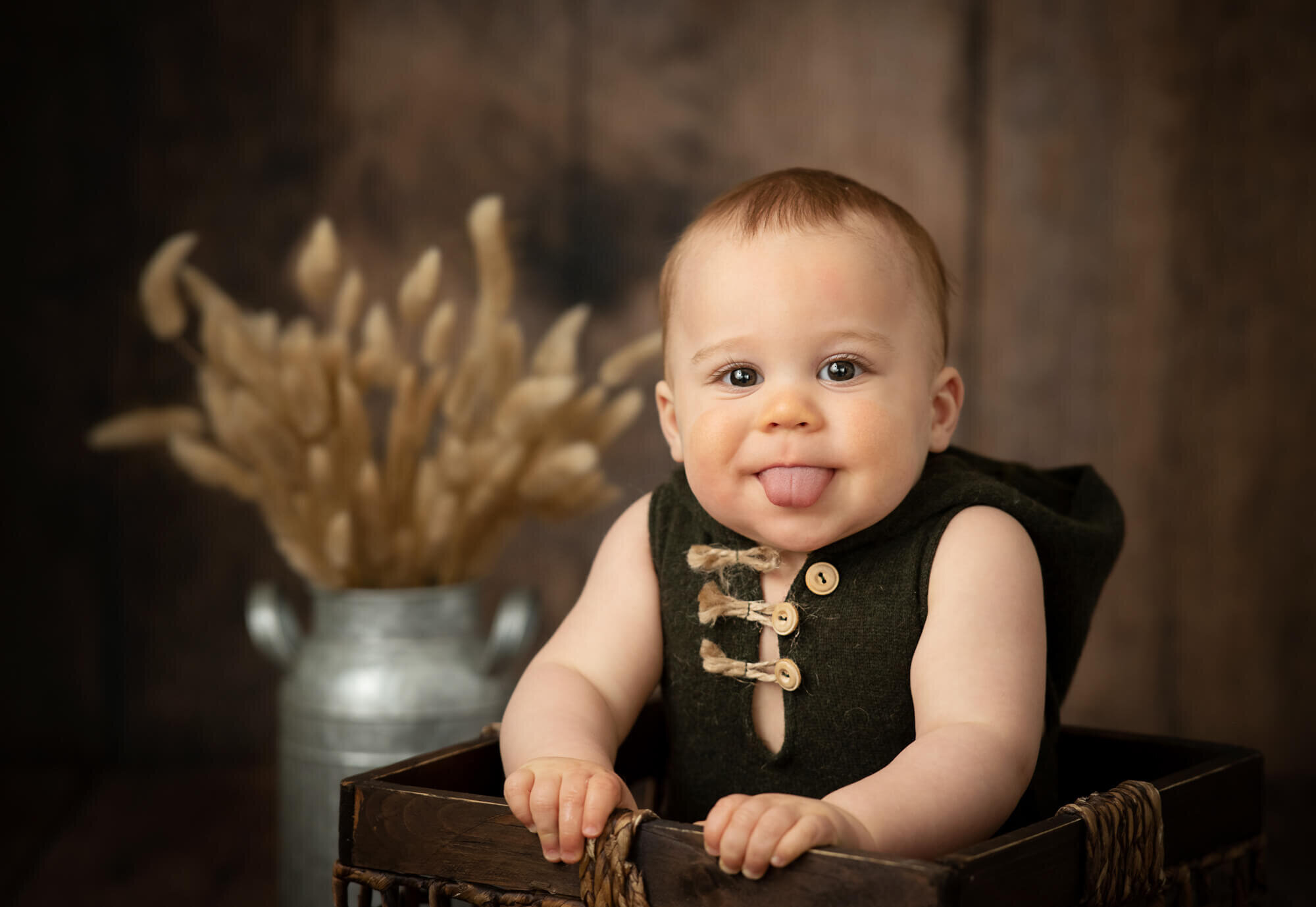 8 month old baby boy in olive romper in basket with tongue out