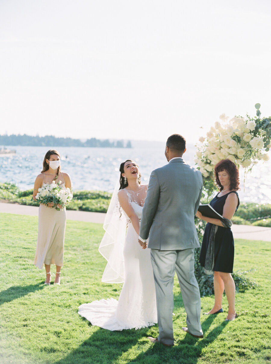 bride laughs hysterically during lakefront wedding ceremony outside on grass