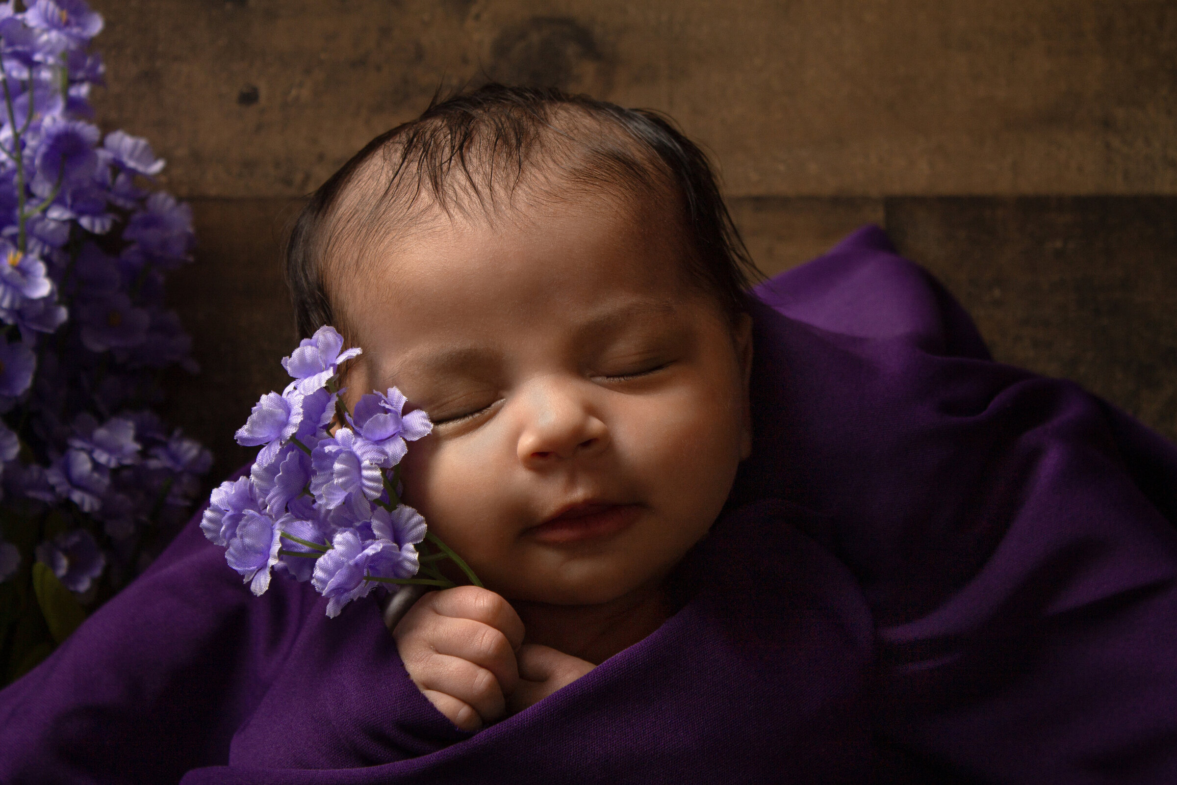 Sleeping newborn holding onto lilacs.