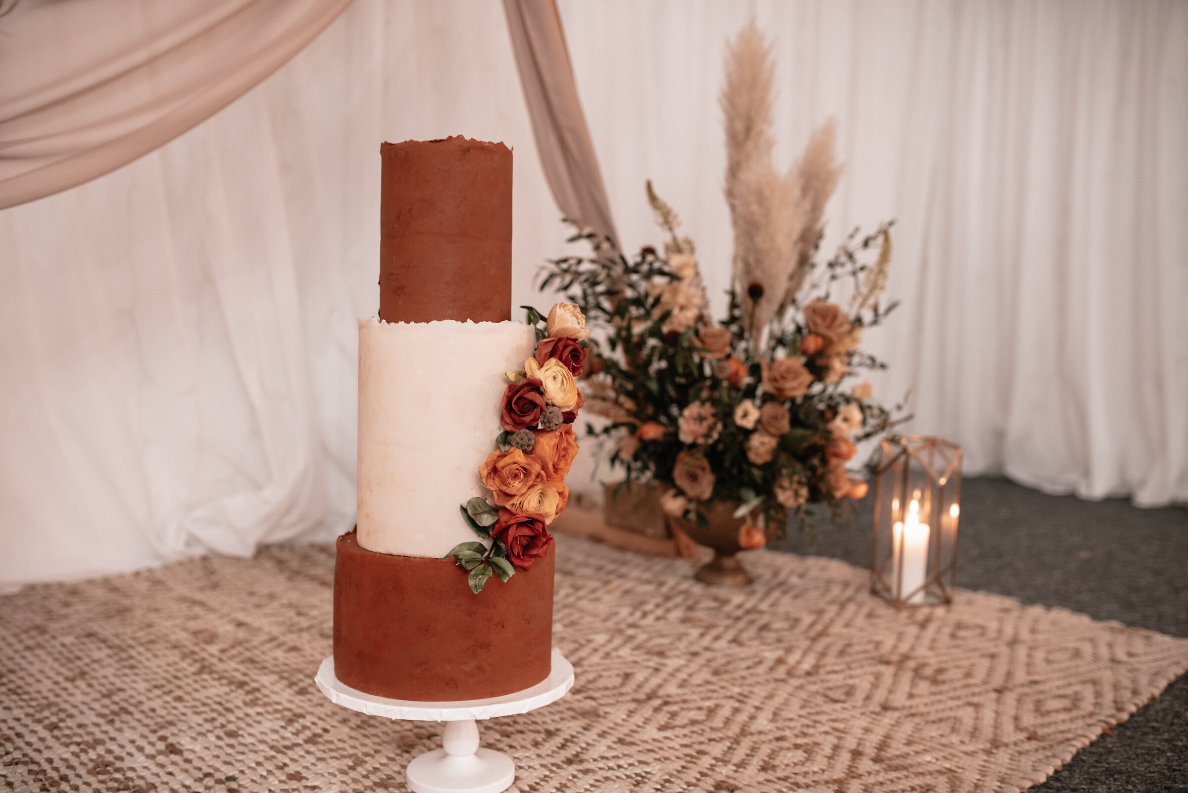 Three tiered wedding cake on stand in front of wedding ceremony floral arrangement