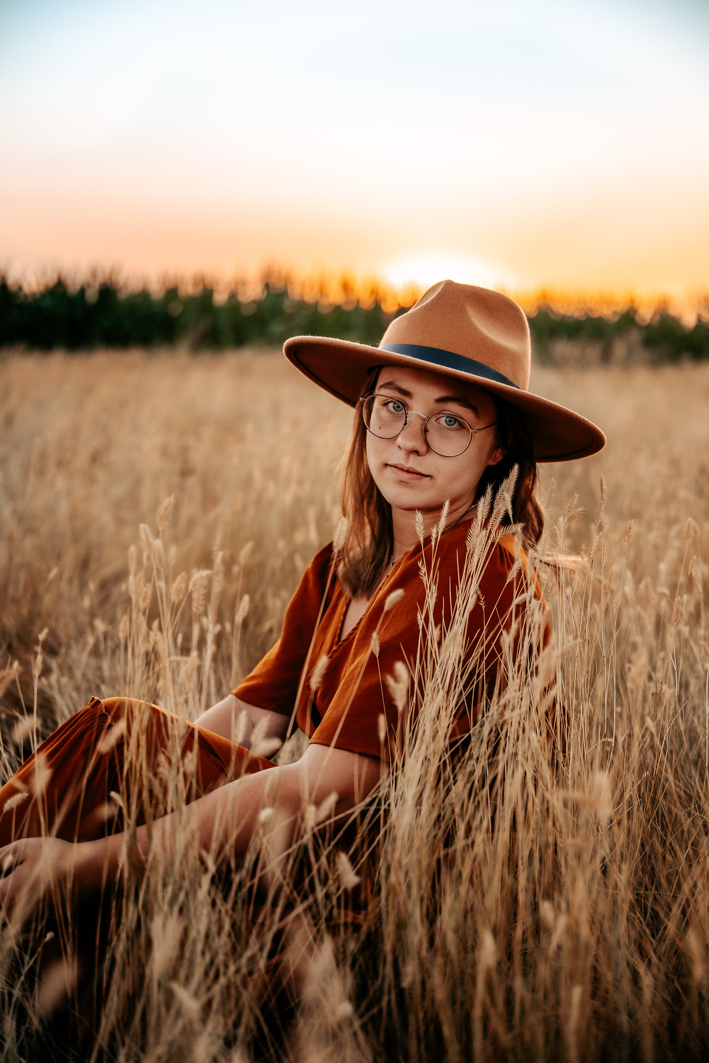 Girl sits in field in felt hat by corn field