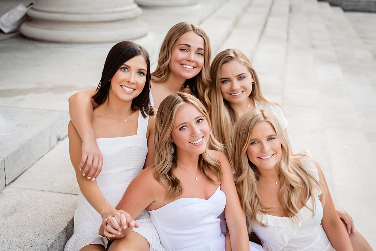 Group photo of 5 Vanderbilt seniors wearing white dresses, sitting on the stairs of a Vandy building