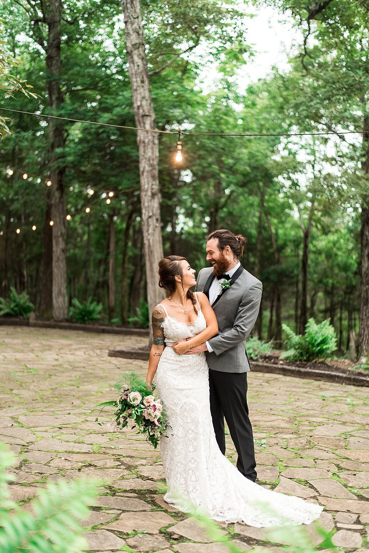 Groom wearing a grey tux jacket standing with his bride under bistro lights on the Stone Gate Farm courtyard patio