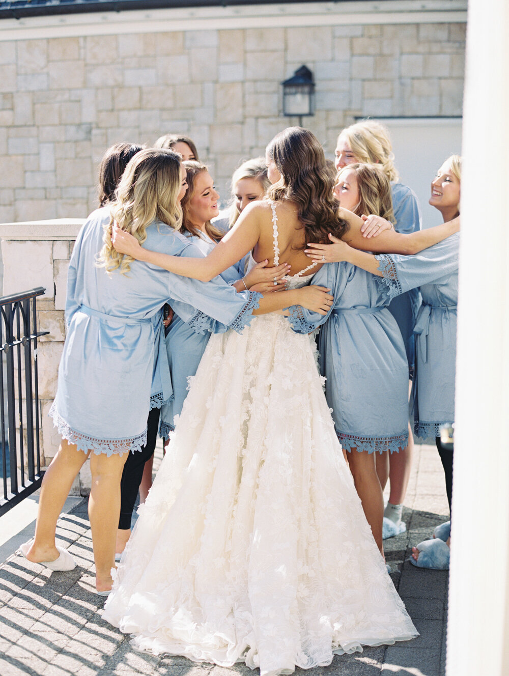 bridesmaids in blue robes hugging the bride on a balcony