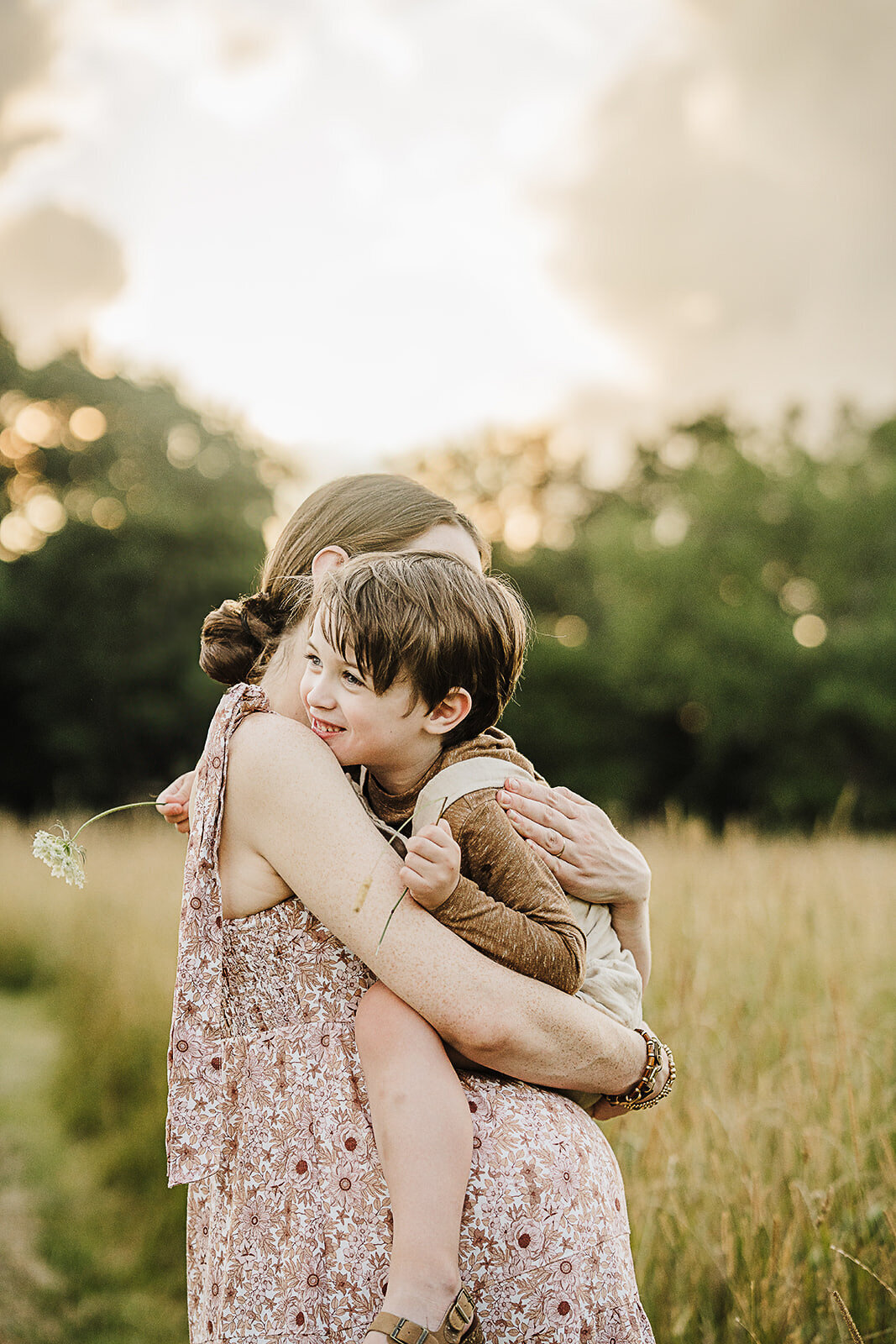 pregnant mom holds toddler close in a boston field at sunset