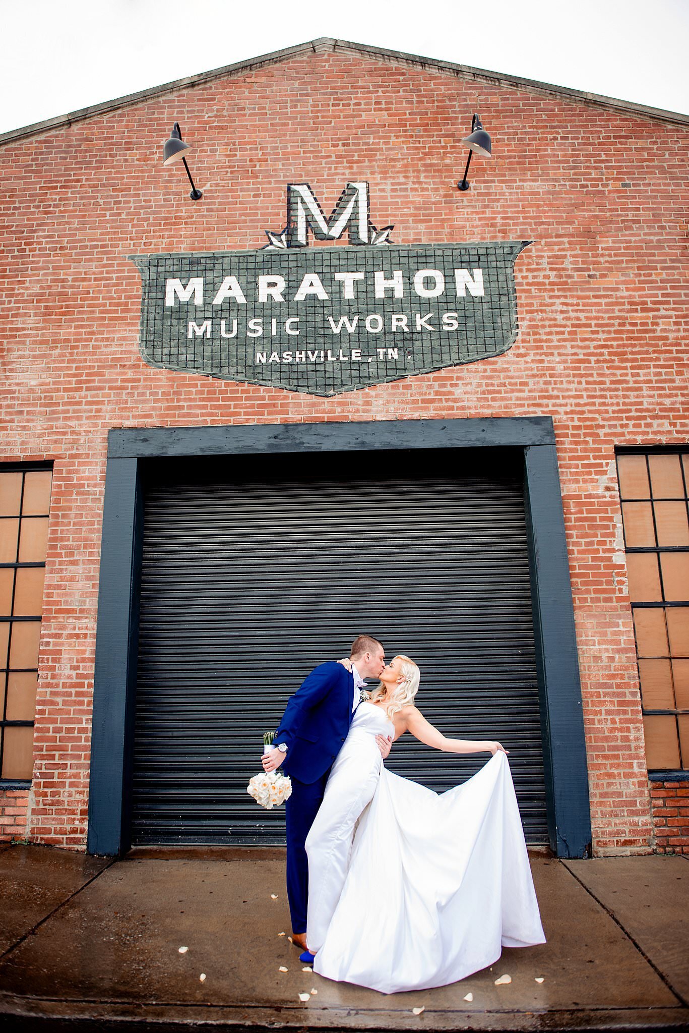 Bride and groom kissing under the Marathon Music Works mural on the brick building