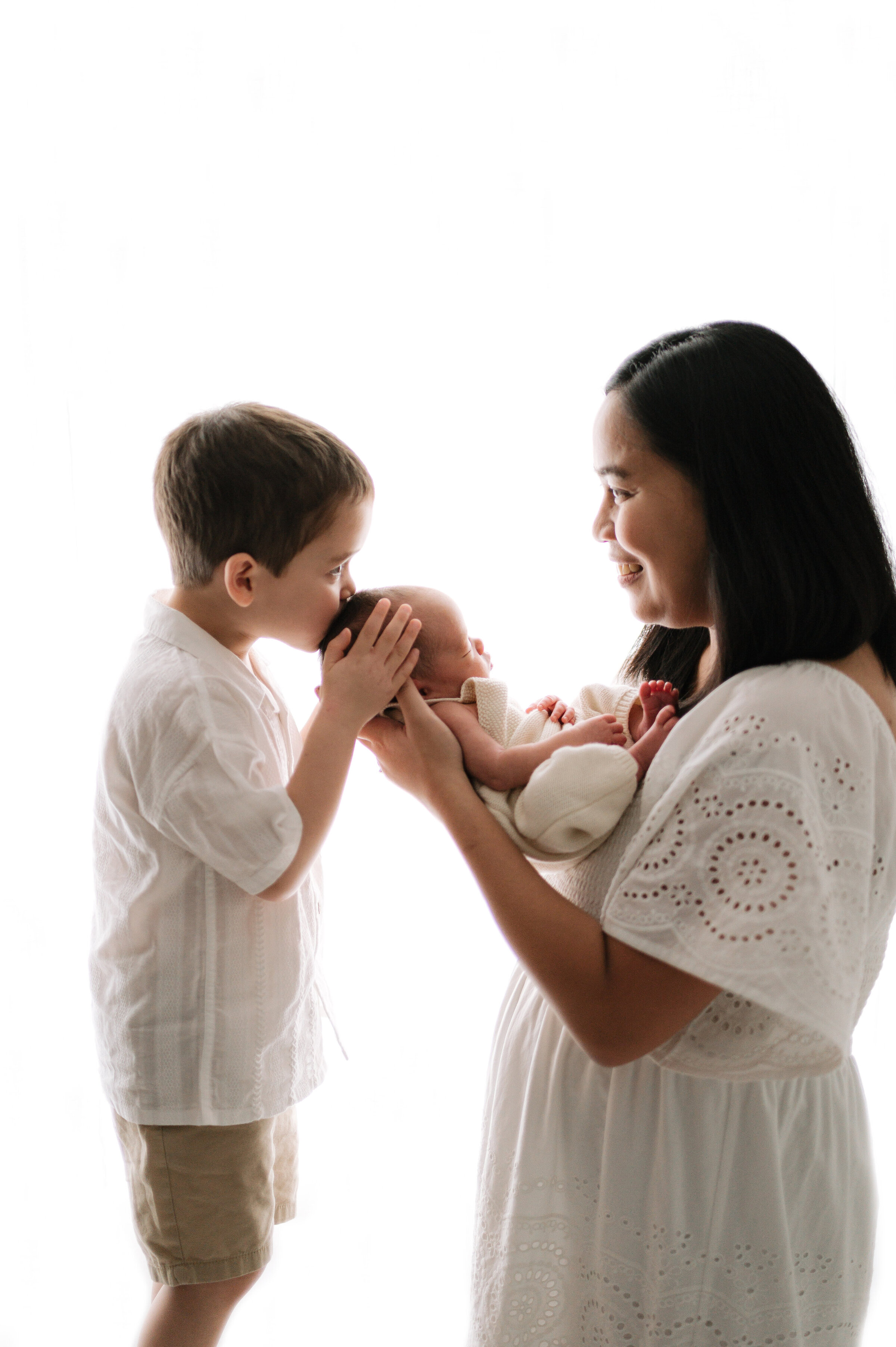 Little boy kissing his newborn sister on the head at a newborn photoshoot in Billingshurst