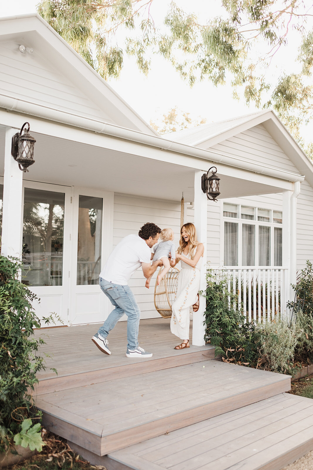 dad swinging baby towards mum at front porch