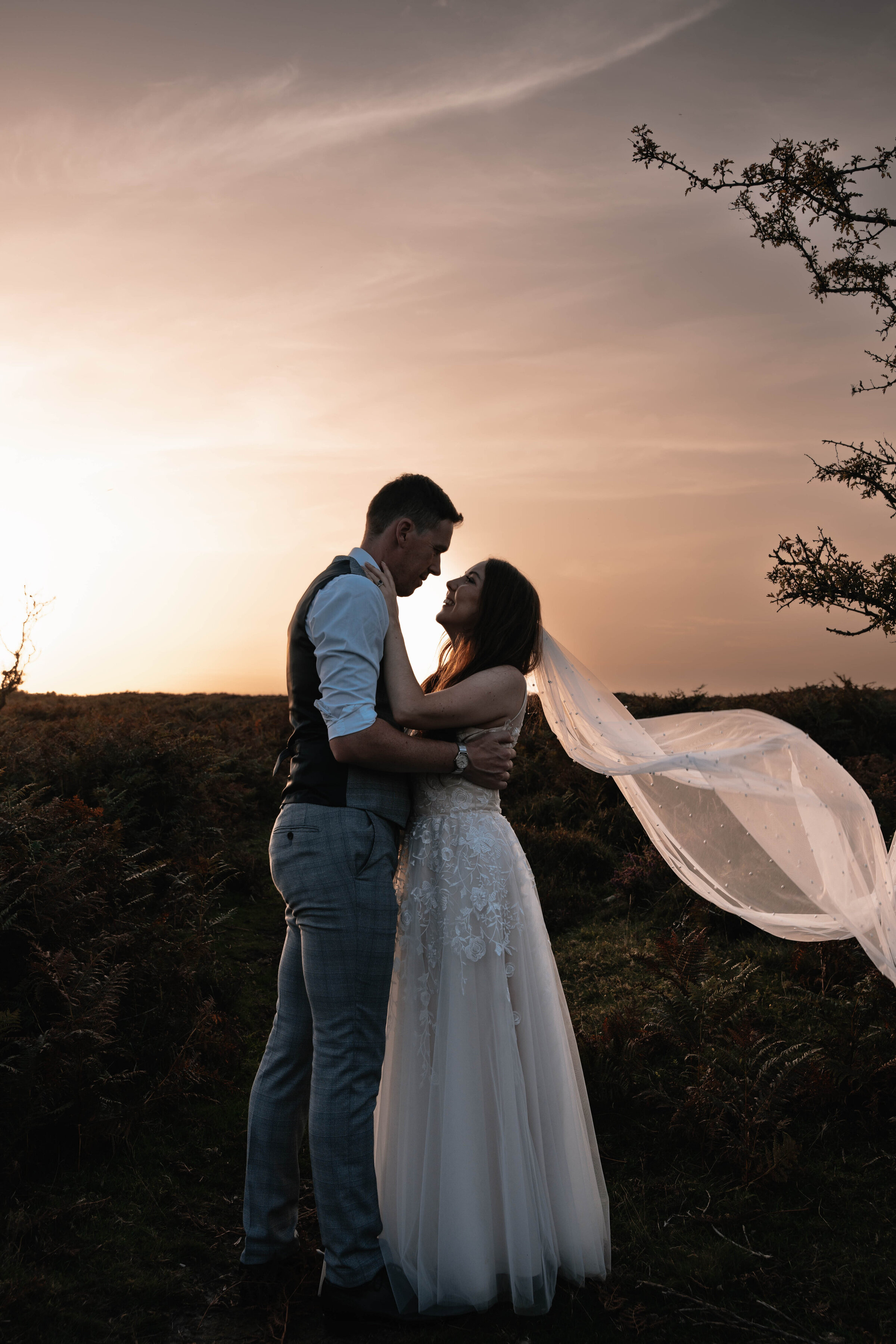 Bride and Groom in wedding attire embracing in front of golden sunset