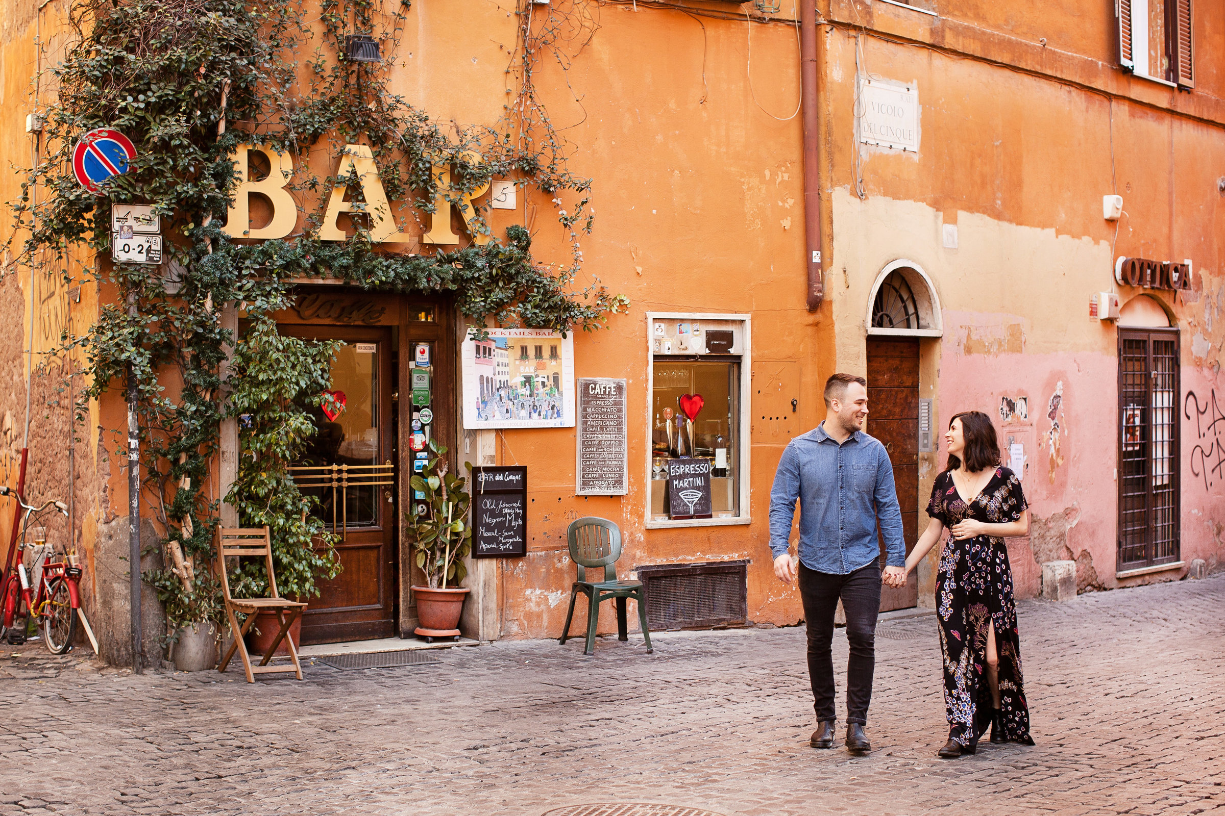 Maternity photo shoo of a pregnant woman and husband walking down a street a classic roman street in Trastevere. Taken by  Rome Photographer, Tricia Anne Photography.