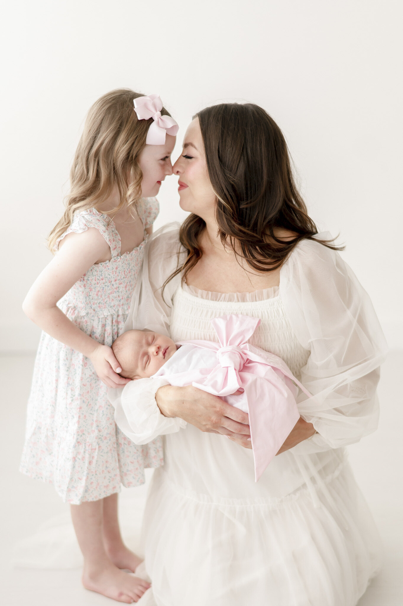 mother and daughter smile at each other over a newborn baby sister