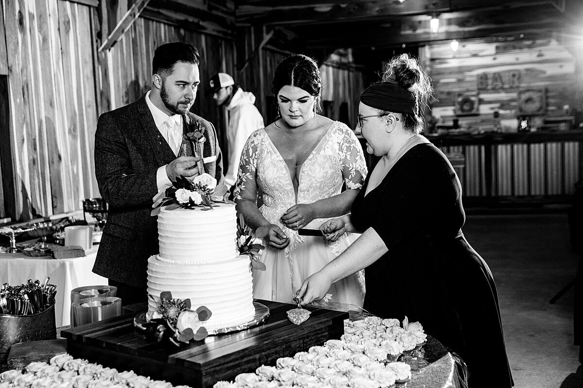 Black and White photo of Mahlia helping the newlyweds cut their wedding cake