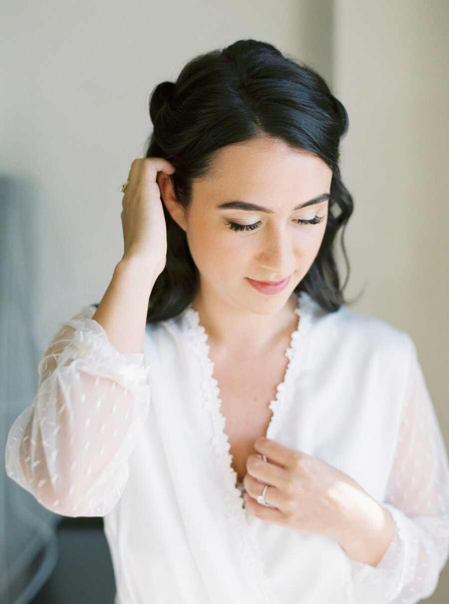 bride in white robe rucks her black hair behind her ears