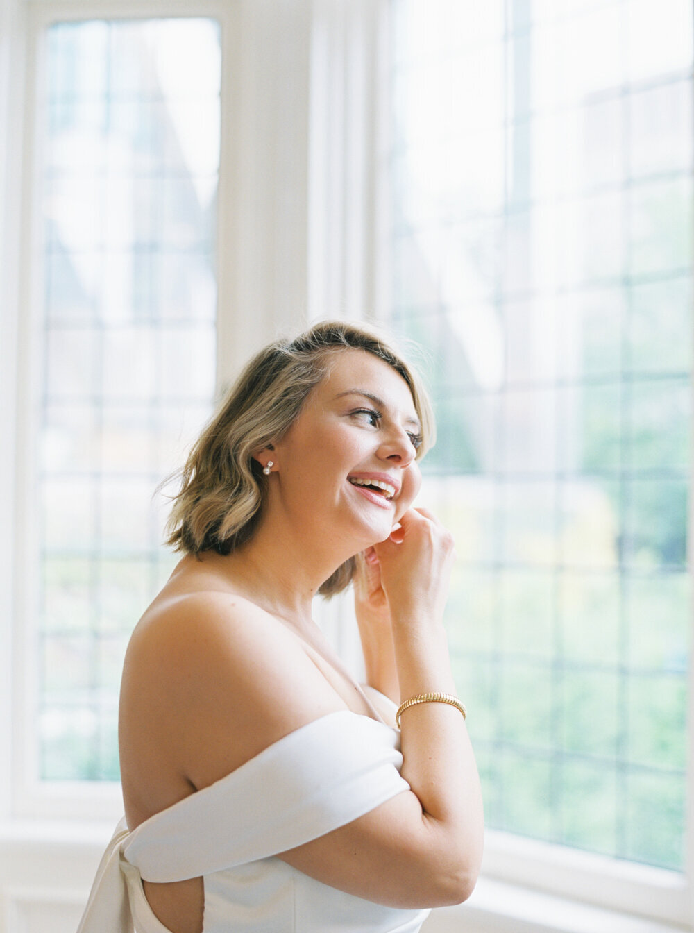 bride putting earrings on by a large window