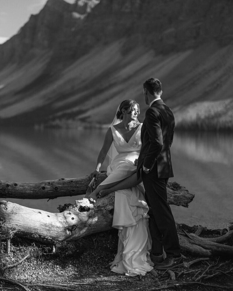 A romantic moment as the groom gazes at his bride while she looks toward the golden evening sun at Bow Lake in Banff National Park. The warm glow of sunset enhances the stunning natural backdrop, creating a timeless and breathtaking portrait of love.
