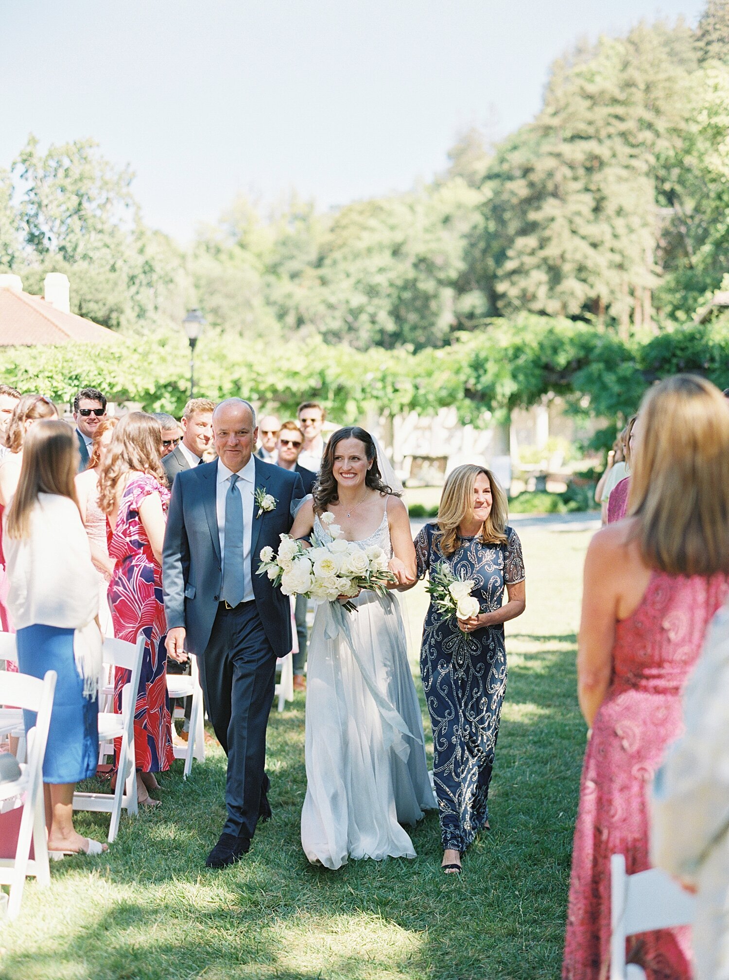 bride in light blue dress walking down the aisle with mom and dad