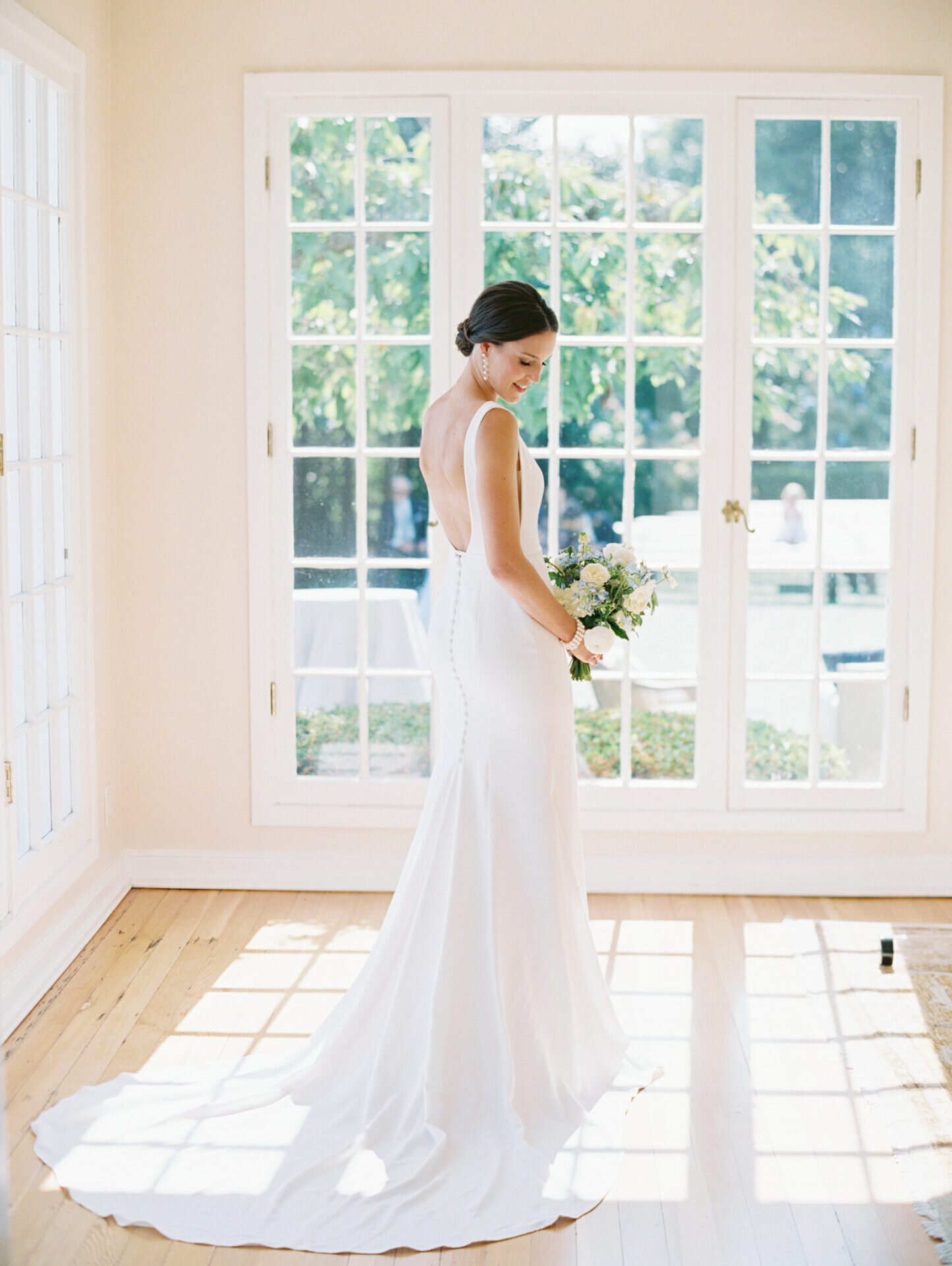 full body portrait of bride in a room full of windows with sun shining through