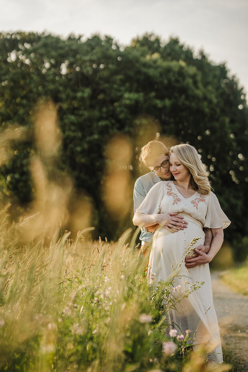 couple embrace during maternity session in a golden field