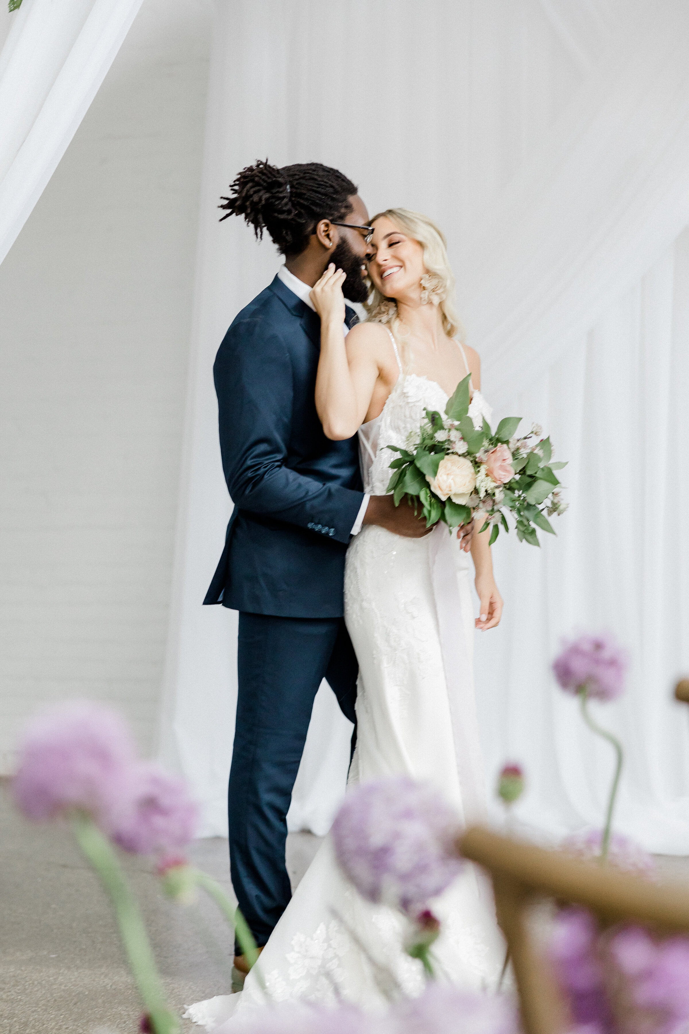 bride and groom snuggling behind floral arrangement