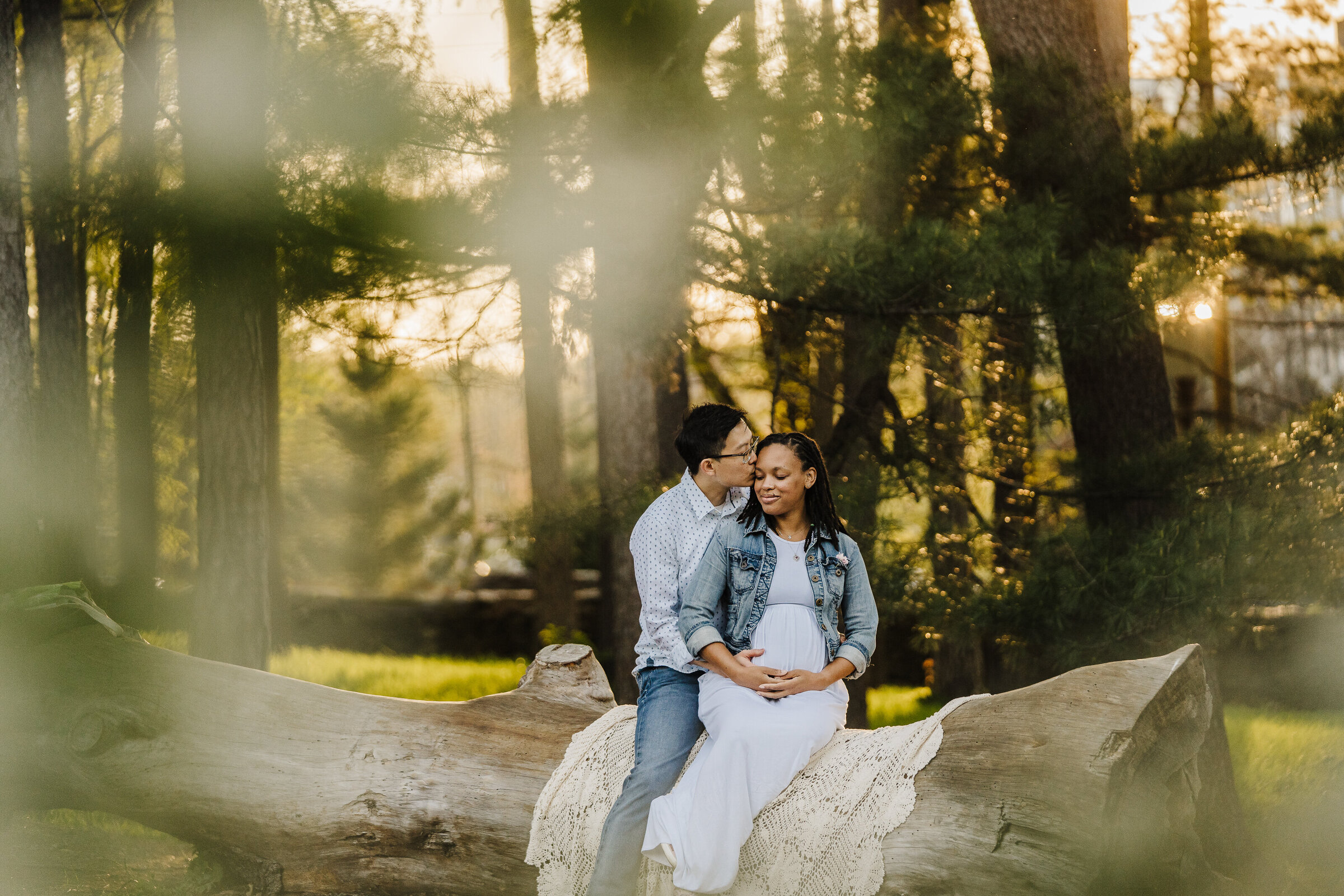 pregnant couple sits on log in forest