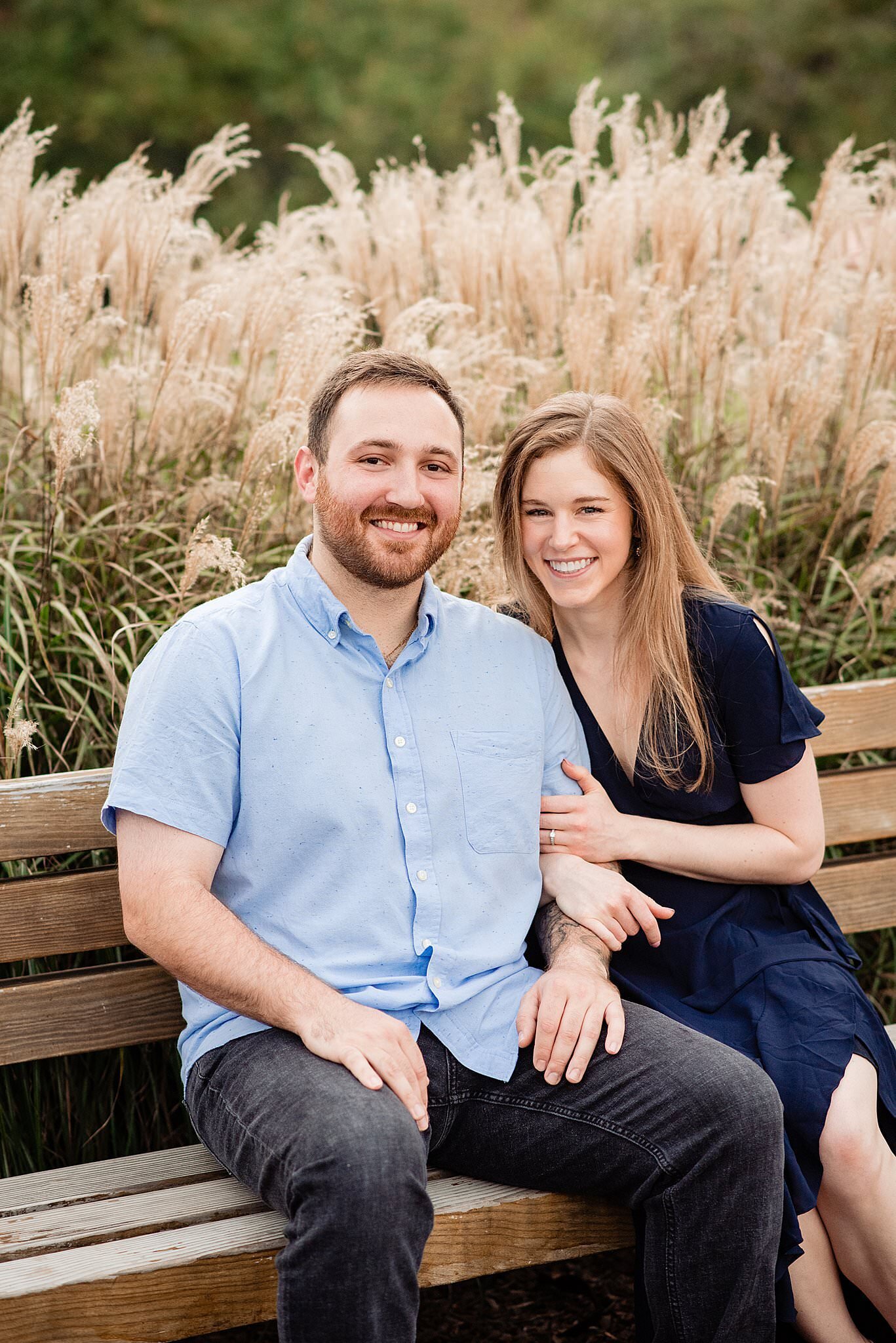 Couple smiling and looking at camera sitting on a bench in front of hay grass in Smith park