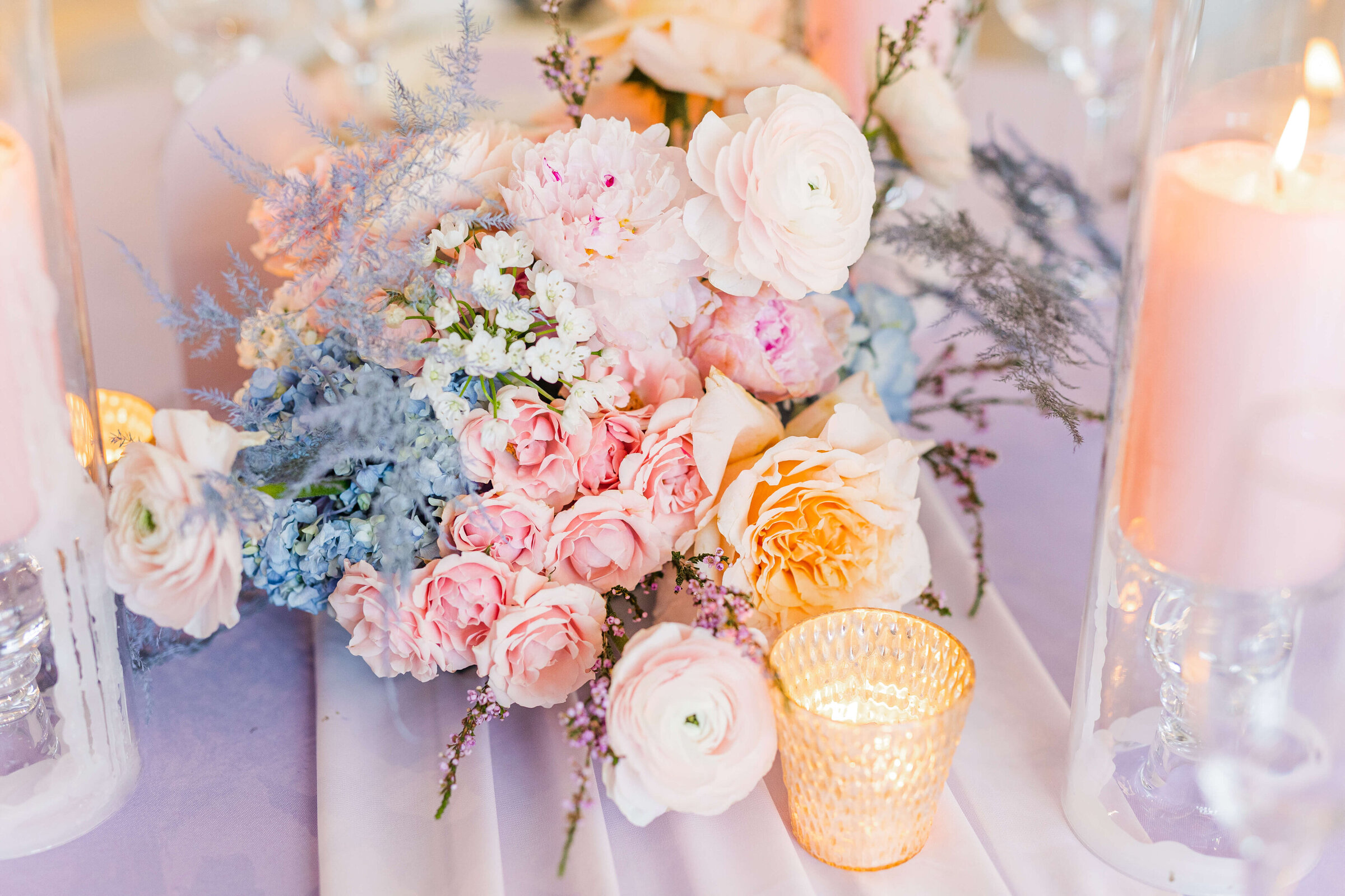 A photo of a wedding bouquet that has pink, blue, white and purple flowers on top of a purple tablecloth