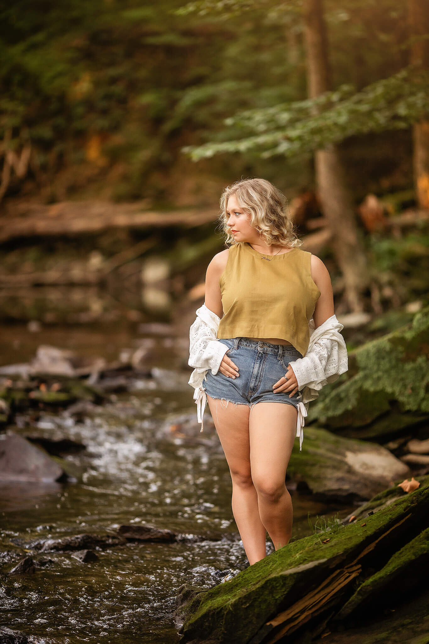 colonel crawford high school senior standing in shallow river wearing jean shorts and yellow top