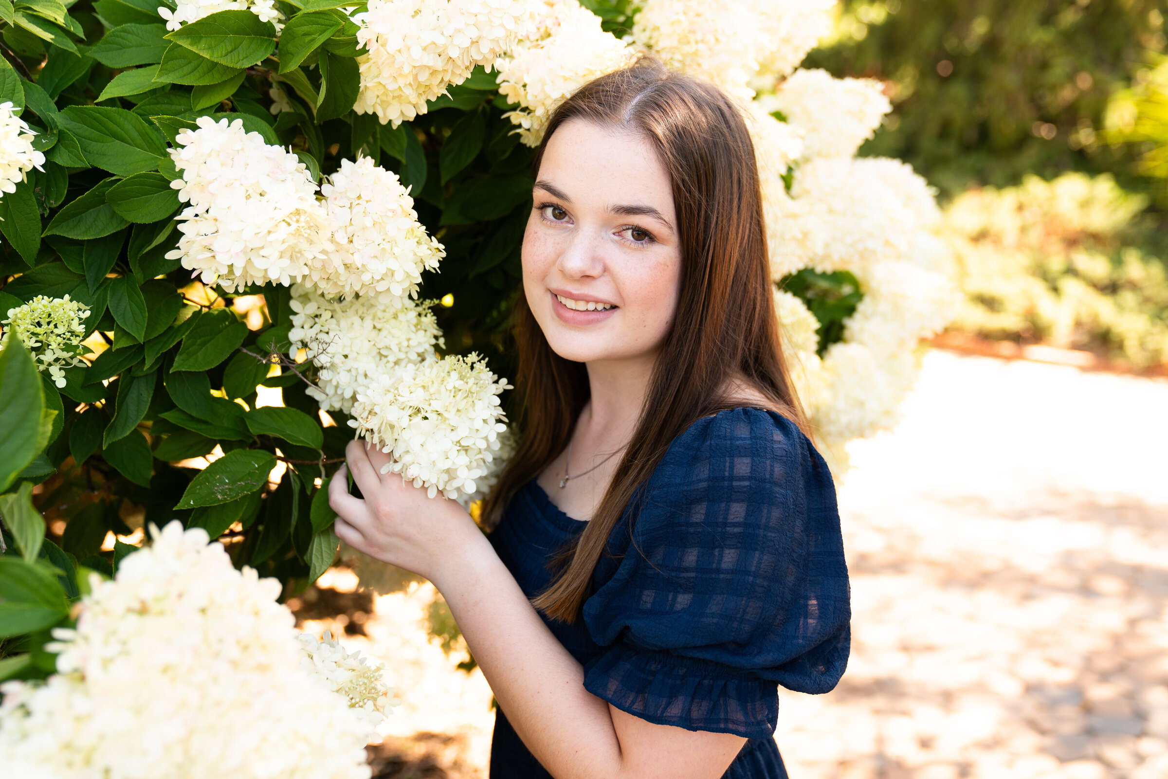 Girl stands next to a hydrangea tree  for her senior photo