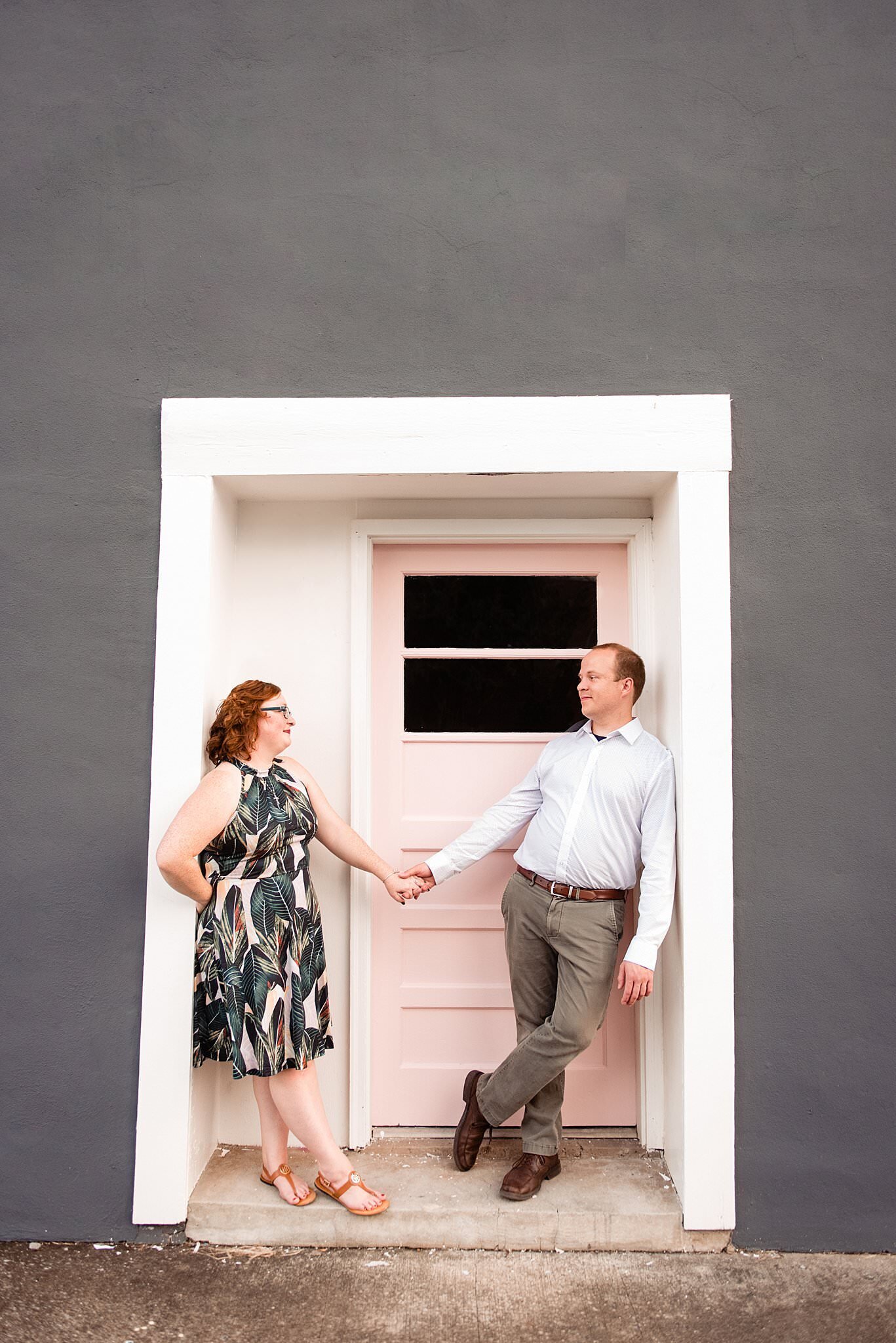 Couple standing apart holding hands in a doorway in downtown Murfreesboro in front of a pink door