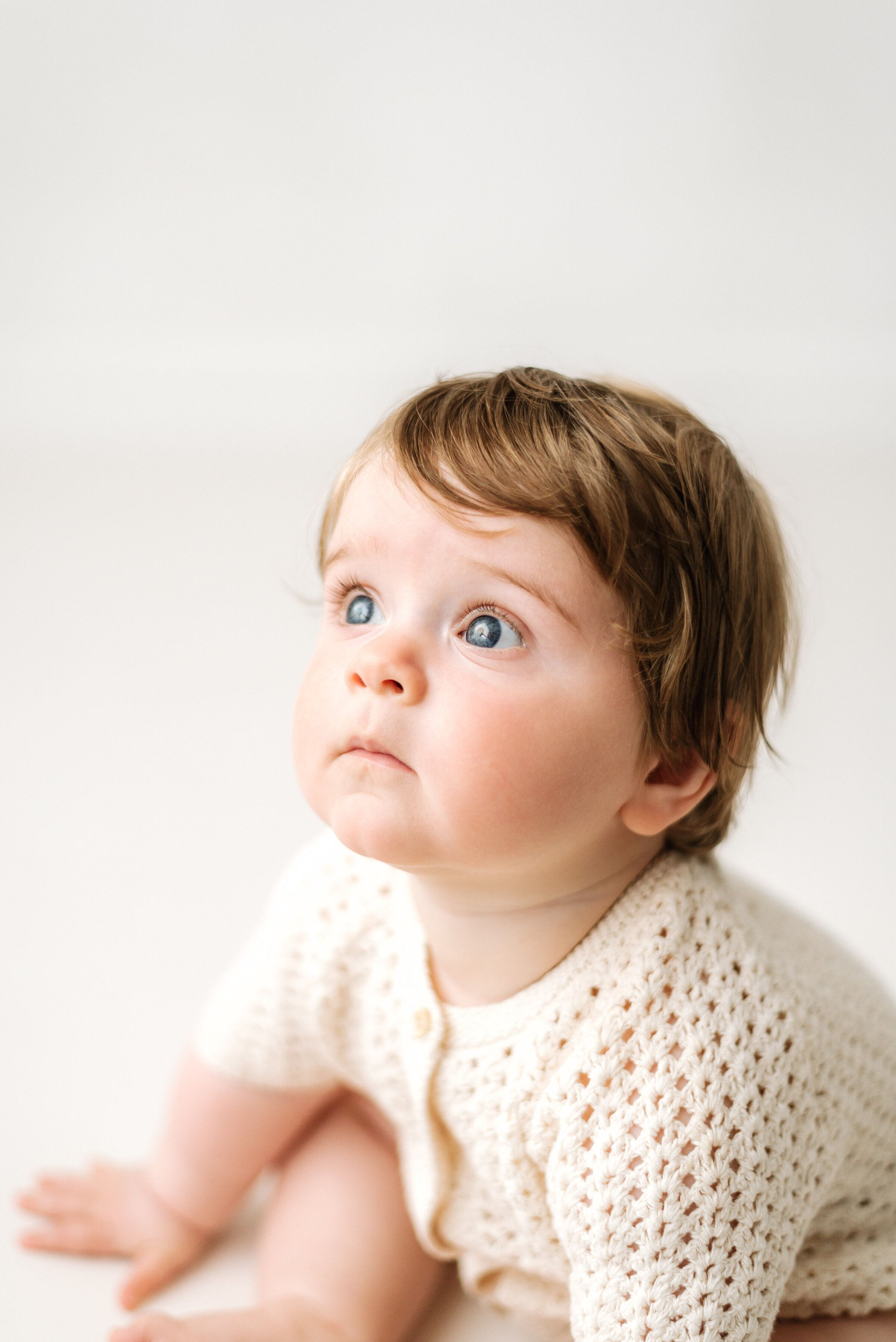 one year old boy sitting down on white floor at milestone photoshoot in Billingshurst