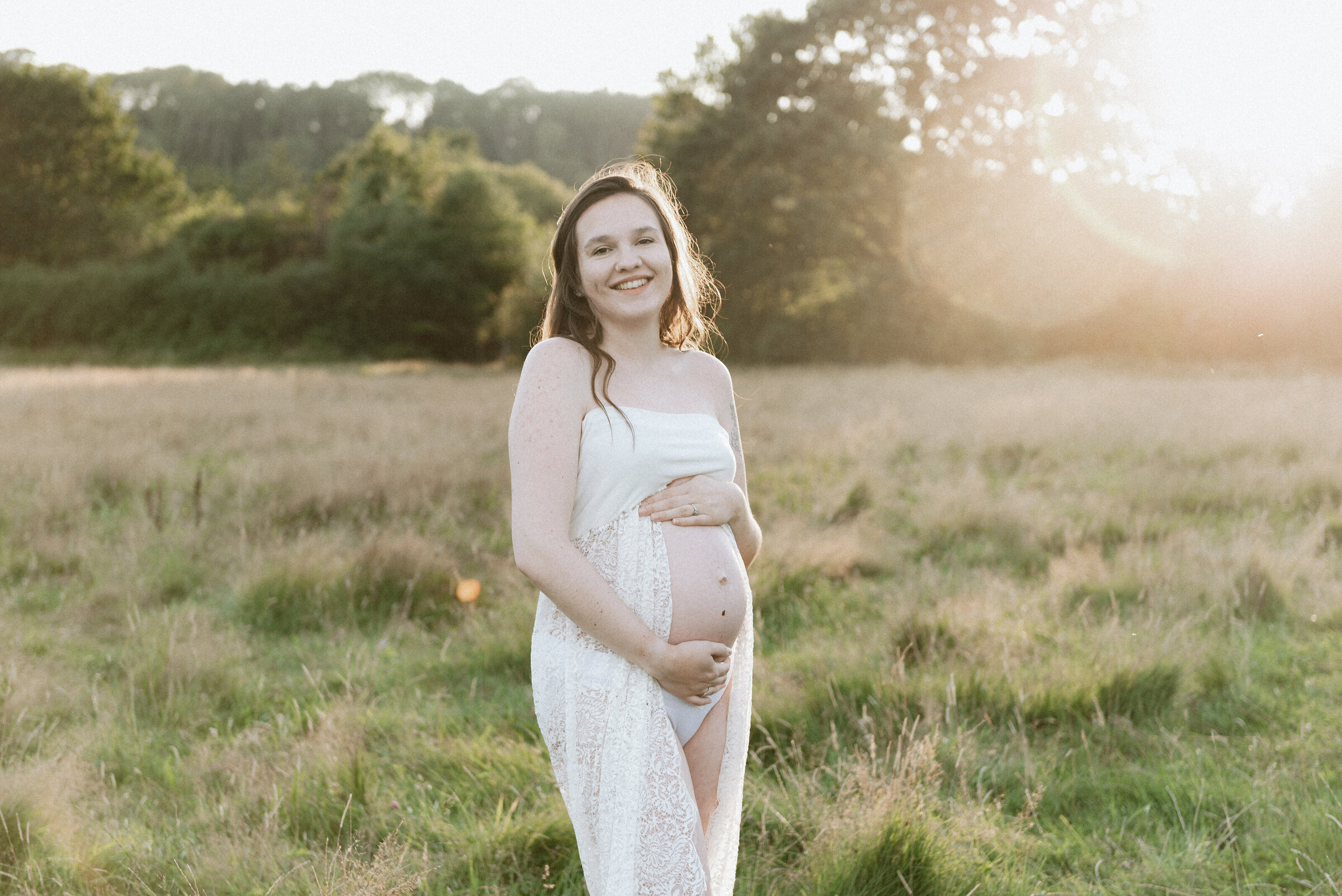 Pregnant mother smiling and holding pregnant belly at maternity photoshoot in Billingshurst