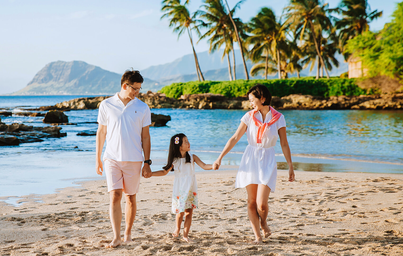 Mum and dad on each side of their daughter holding hands and swinging her higher than ever on Waikiki beach family portrait.