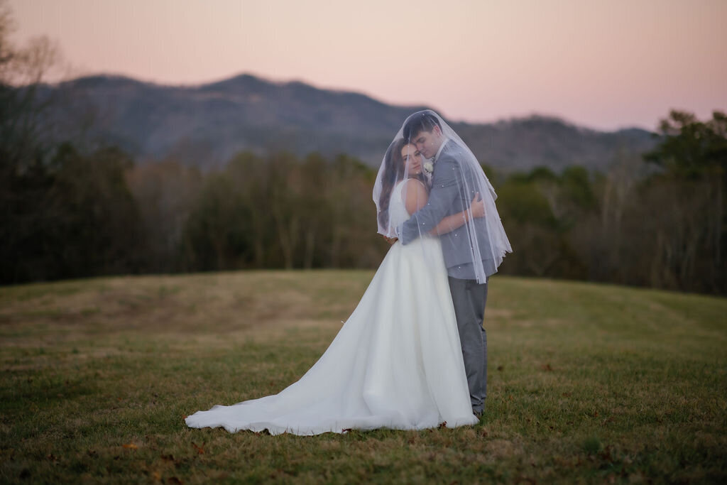 Harpers Vineyard elopement with bride and groom hugging under the brides veil with a pink sky behind the Smoky Mountains in the distance